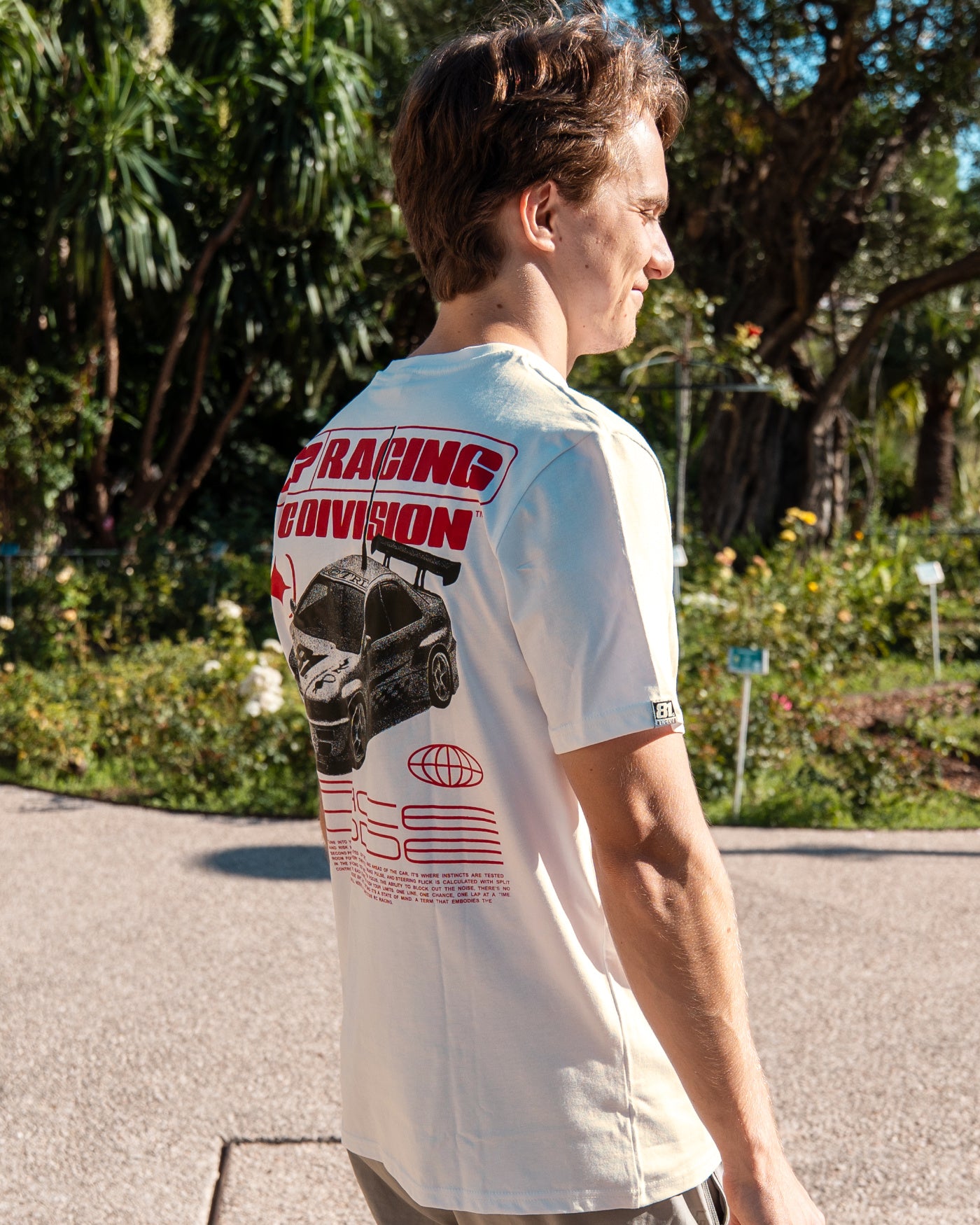 81 CLUB Origins T-Shirt - Off White worn by Oscar featuring RC car design on back in outdoor setting.