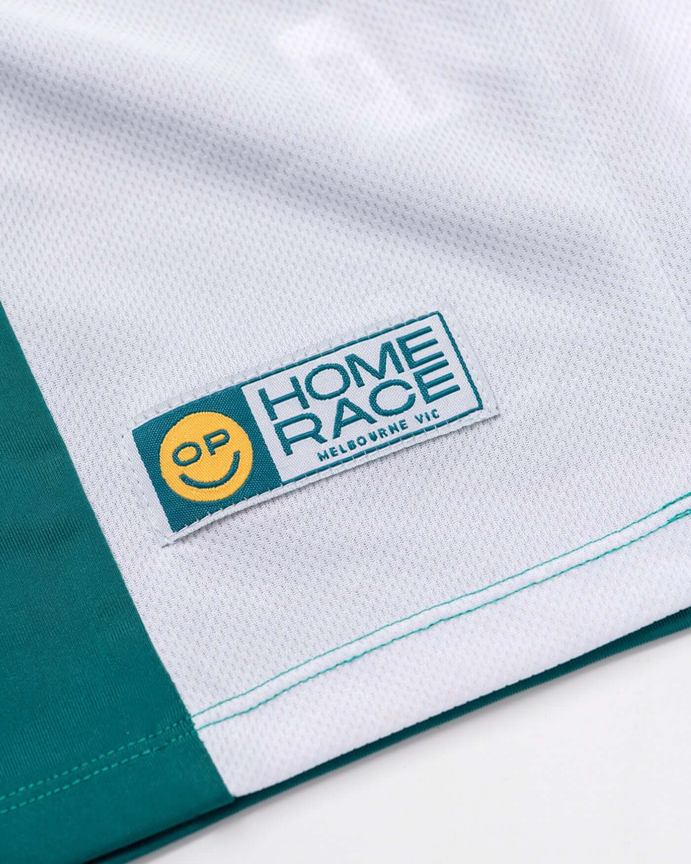 Close-up of the branding on the Home Race '26 Jersey featuring the OP smiley logo and vibrant colors.