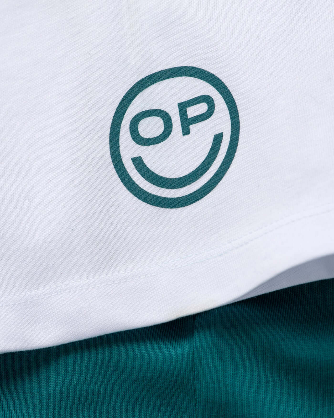 Close-up of the OP smiley motif on the Home Race '26 T-Shirt - Green, featuring bold design elements.