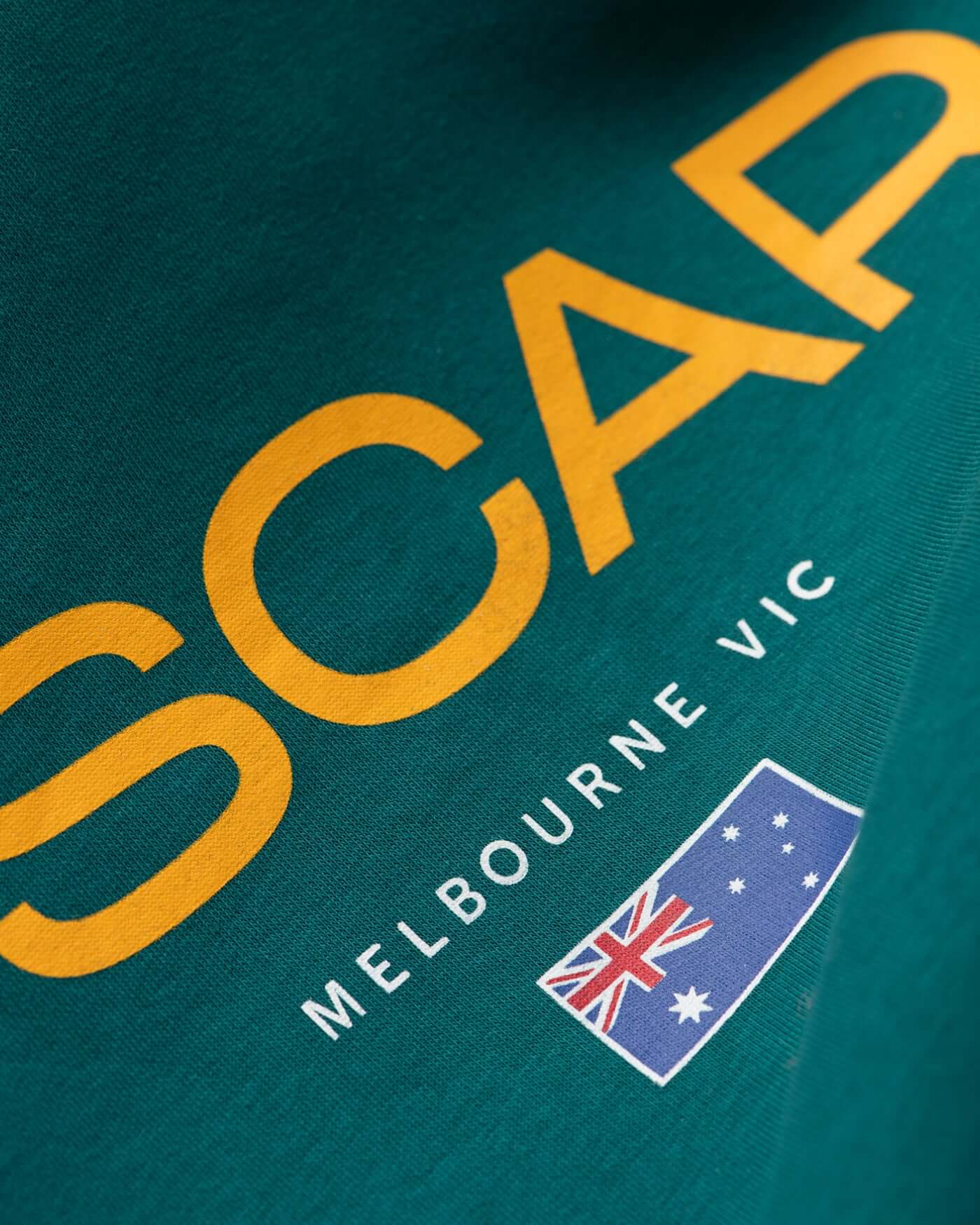 Close-up of Home Race '26 Hoodie - Green fabric showing SCAP Melbourne VIC with Australian flag design.