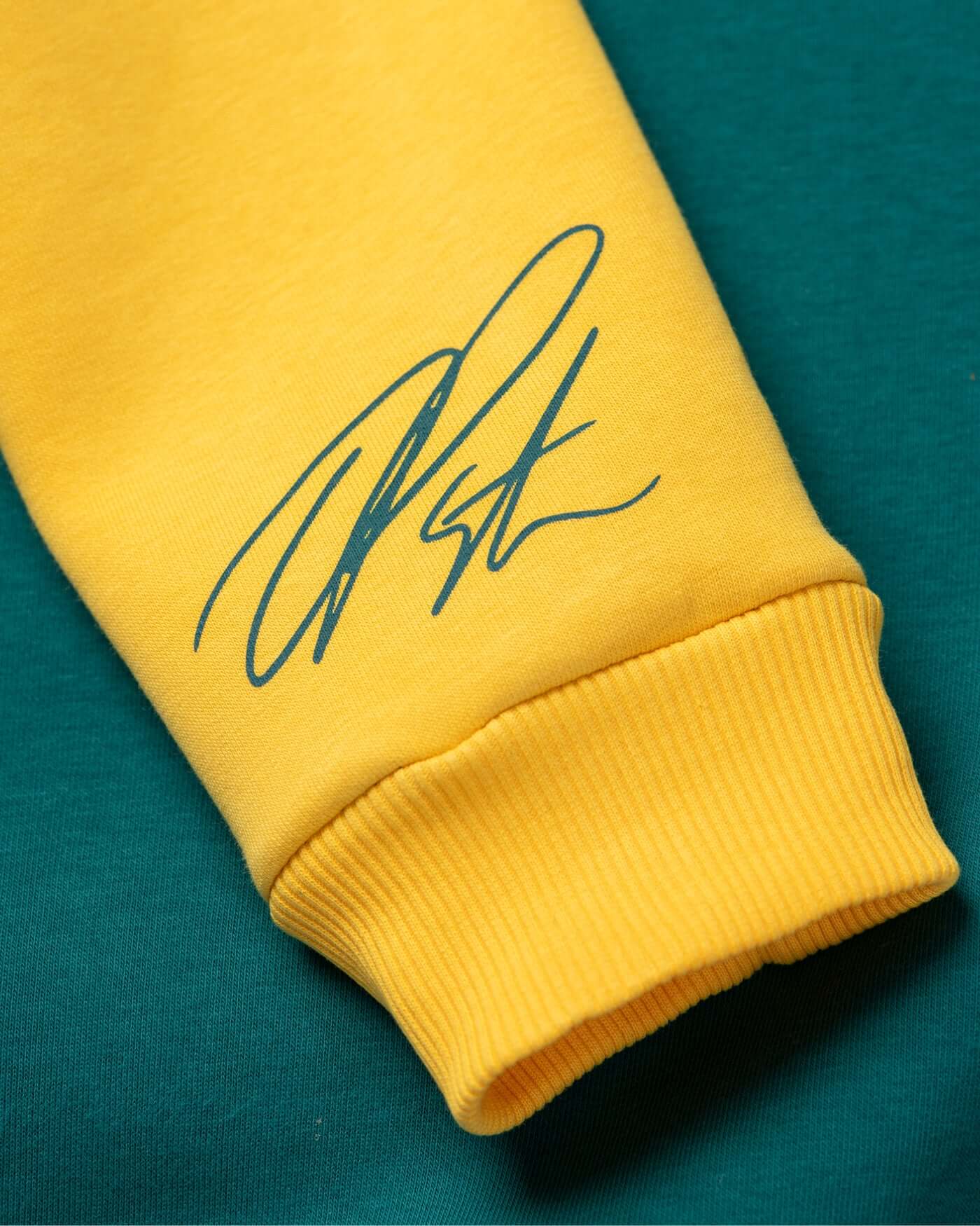 Close-up of the Home Race '26 Sweater sleeve with Oscar Piastri's signature on yellow fabric.