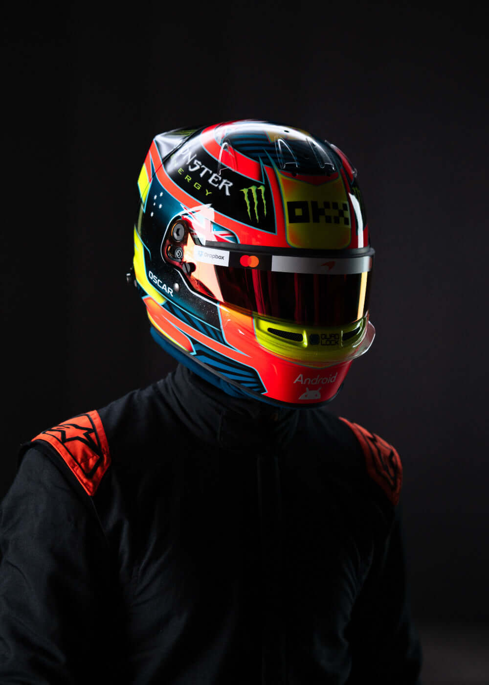 Close-up of a colorful racing helmet with vibrant designs against a dark background, showcasing motorsport style.