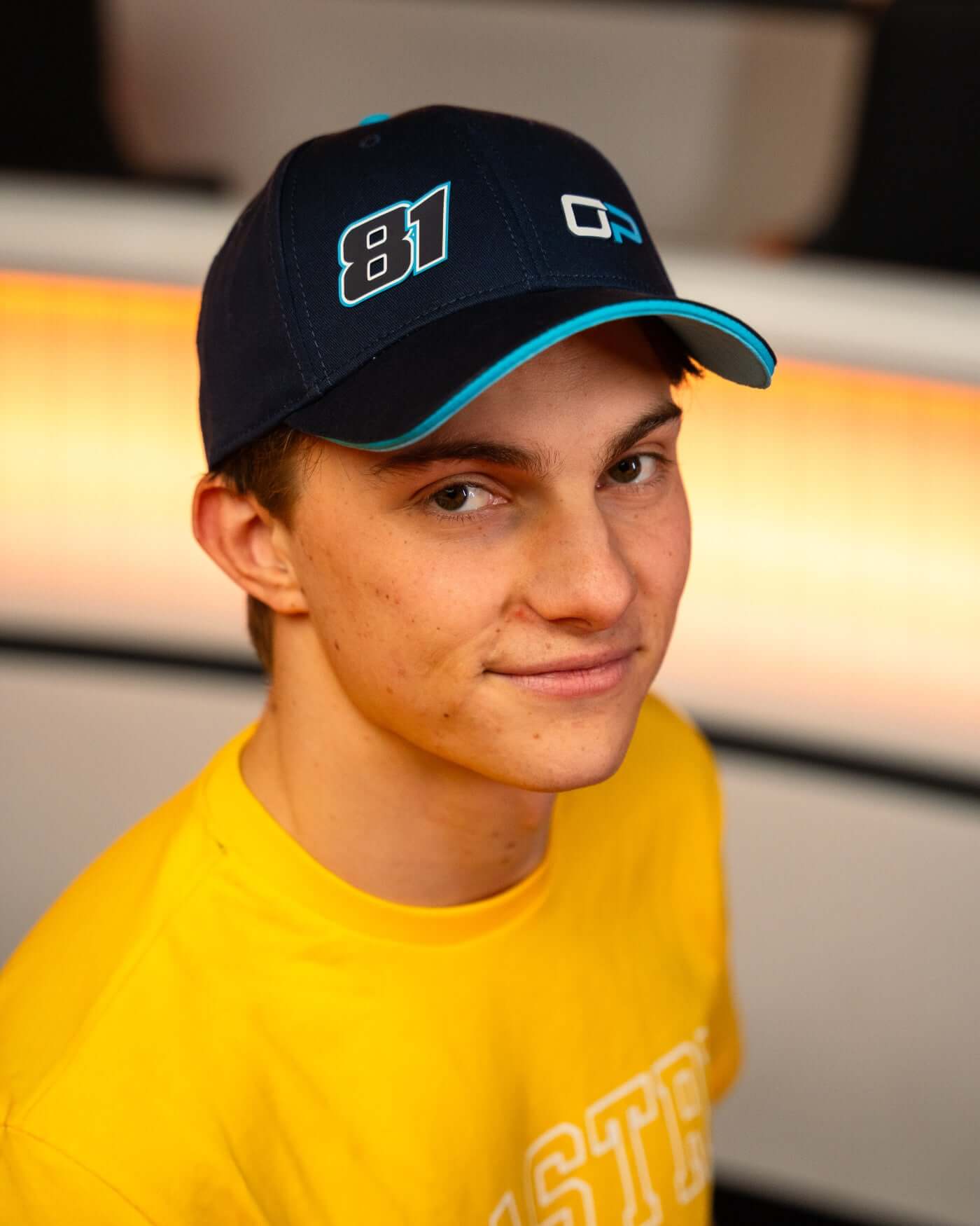 Navy Signature Cap featuring OP logo and race number 81, worn by a young man with a yellow shirt.
