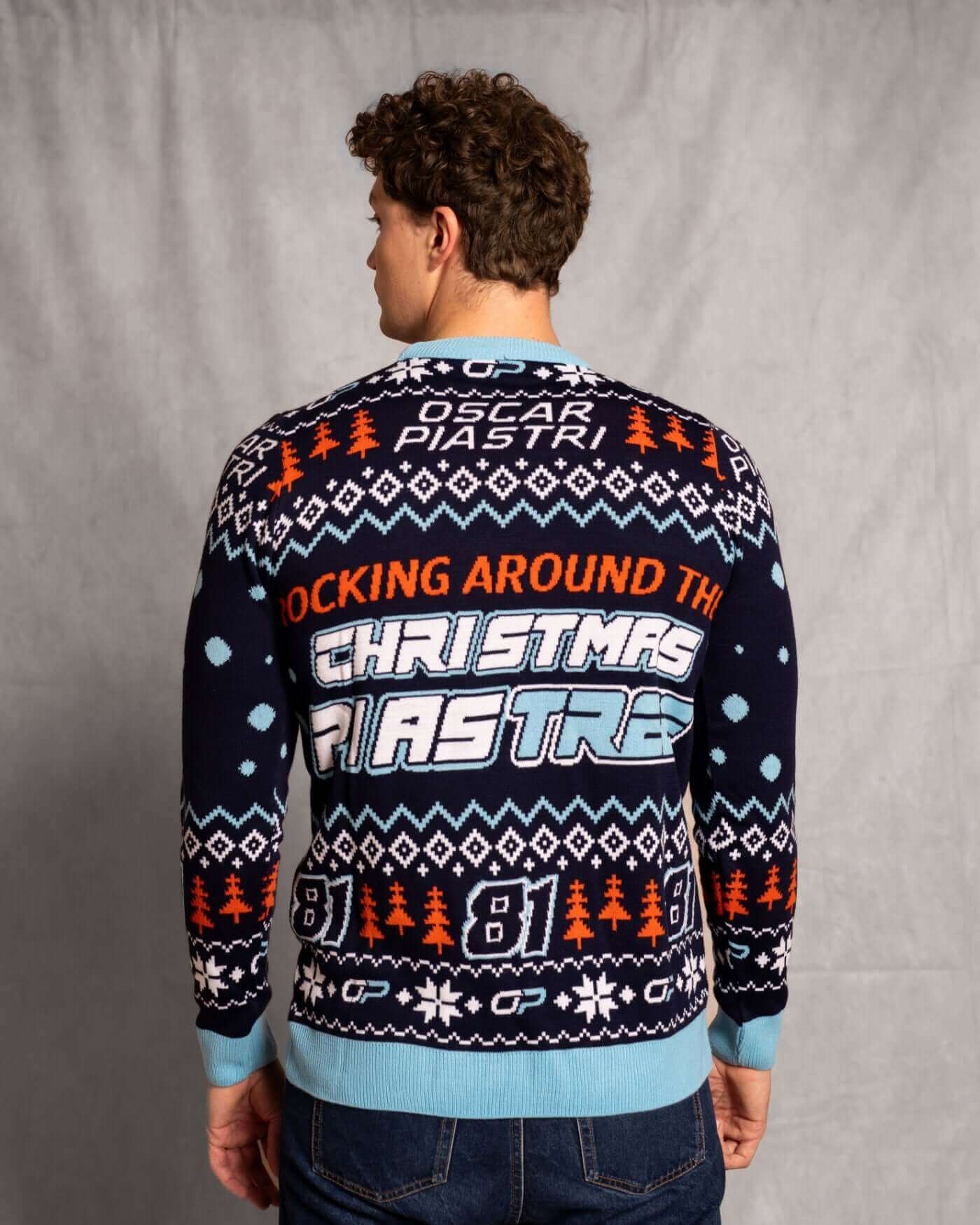 Person wearing Oscar Piastri Christmas sweater with festive design and text "Rocking Around the Christmas Piastree," back view.