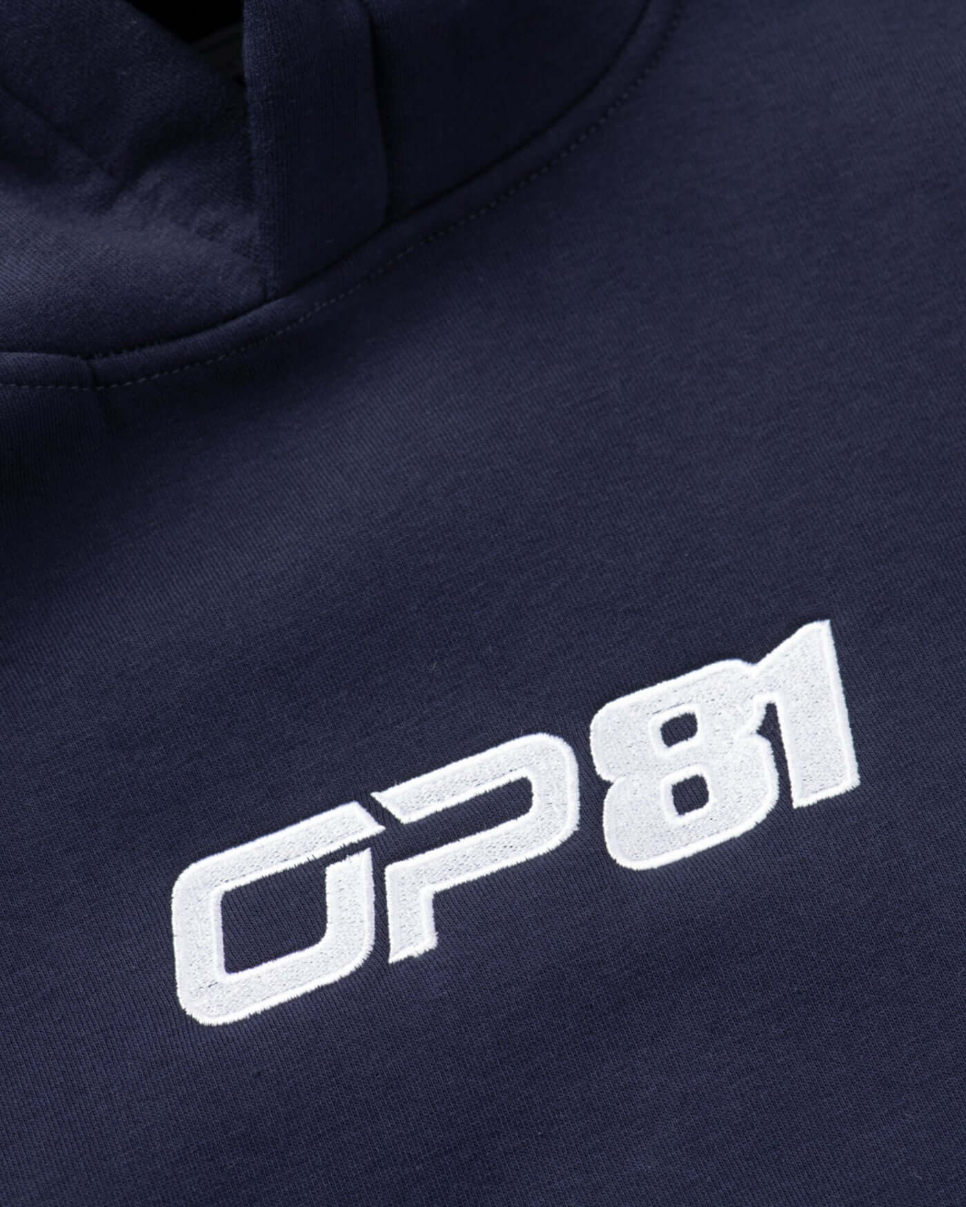 Close-up of OP81 logo embroidered on navy fleece hoodie, showcasing quality and style in apparel.