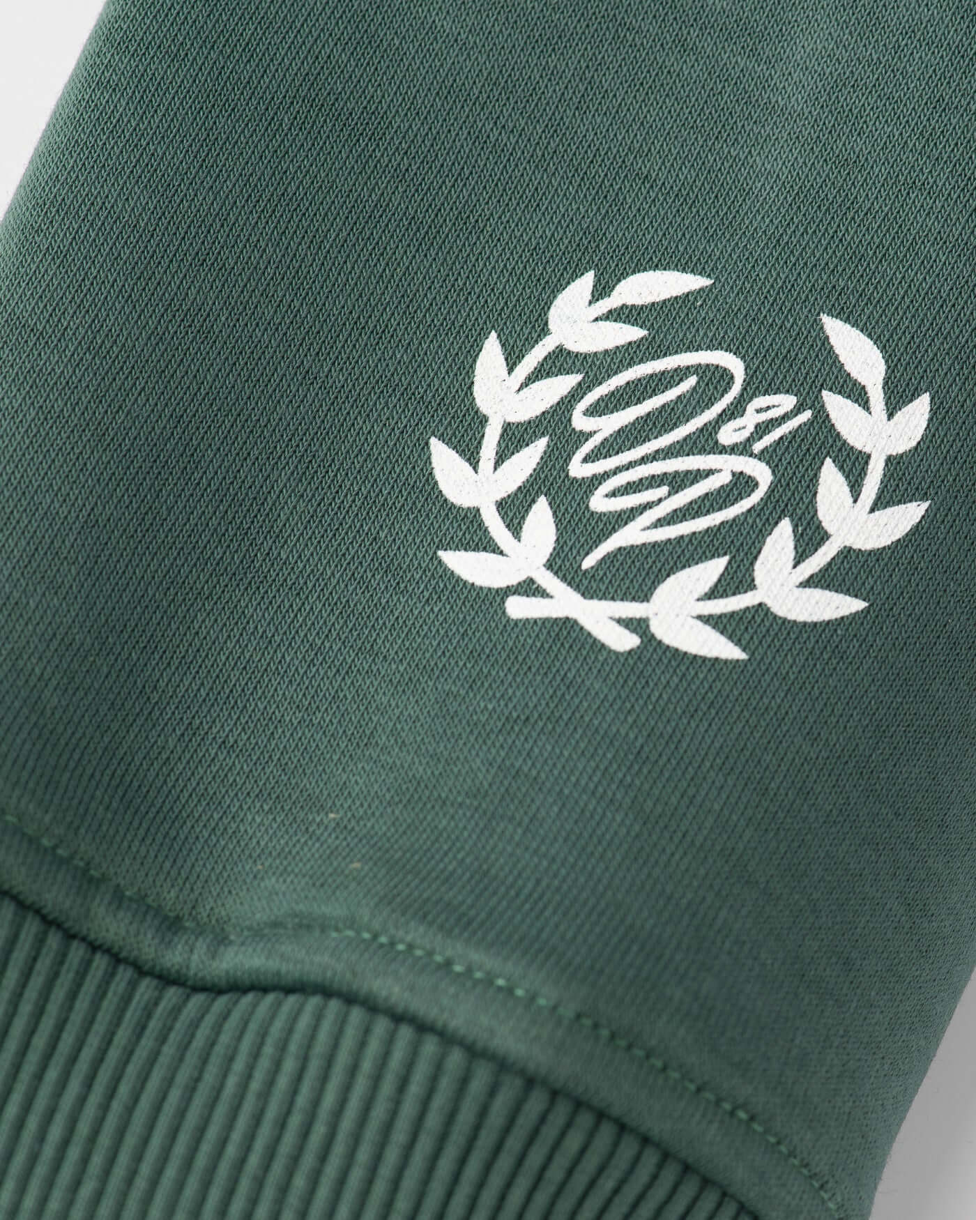 Close-up of the logo on the Home Race Hoodie in green, featuring a laurel design and stylish lettering.