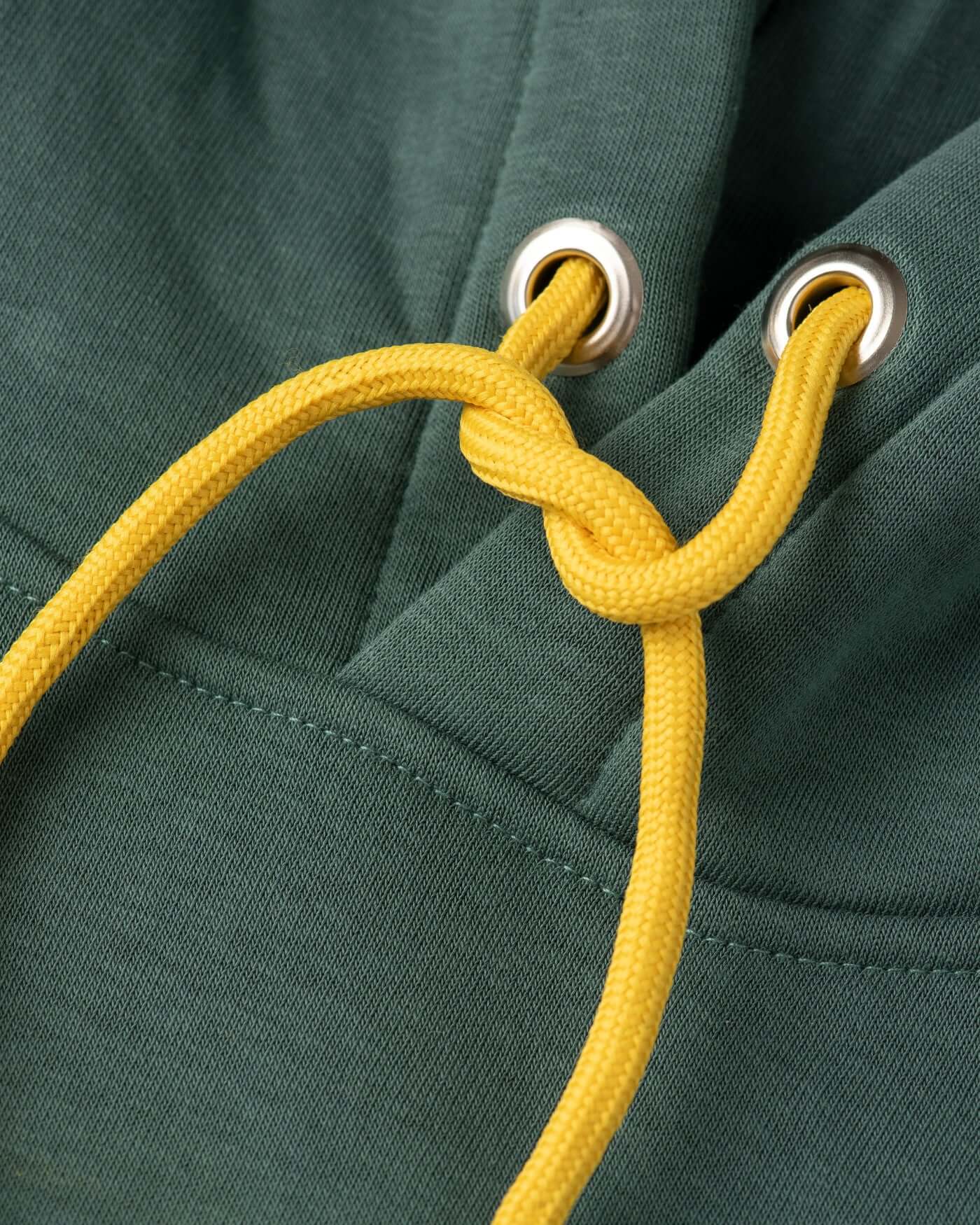 Detail of green hoodie showing yellow drawstrings and eyelets, highlighting its stylish design and cozy fit.