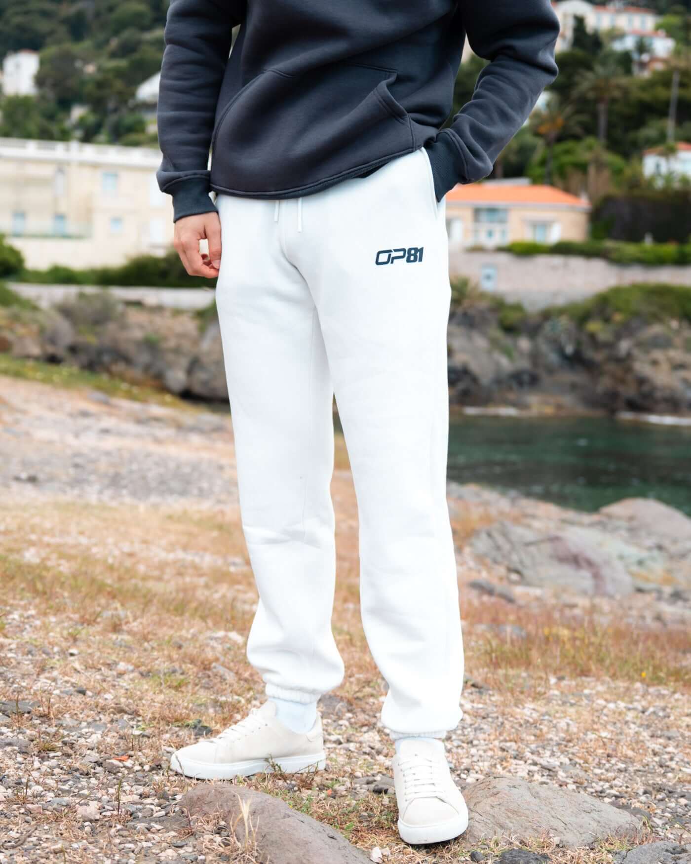 Model wearing Signature Joggers - Off White with OP81 logo patch by the beach.