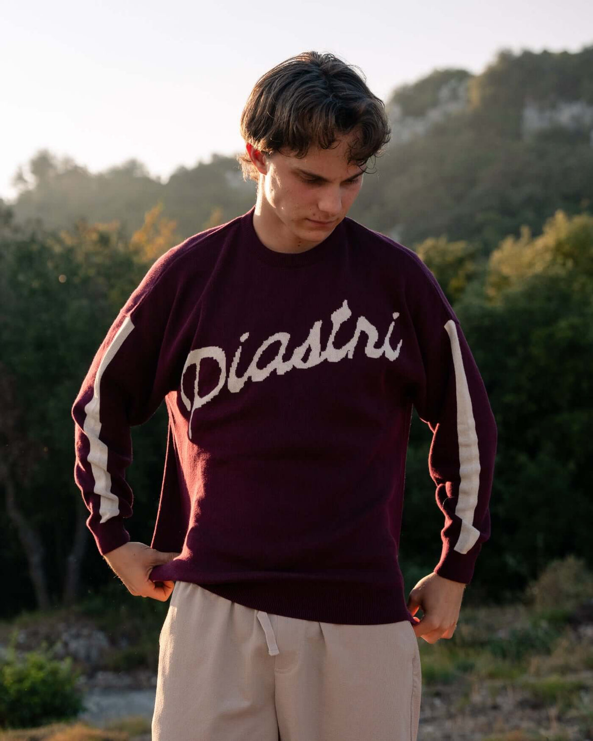 World Circuit Knitted Sweater - Burgundy worn by a model outdoors, showcasing Piastri script and jacquard stripe.
