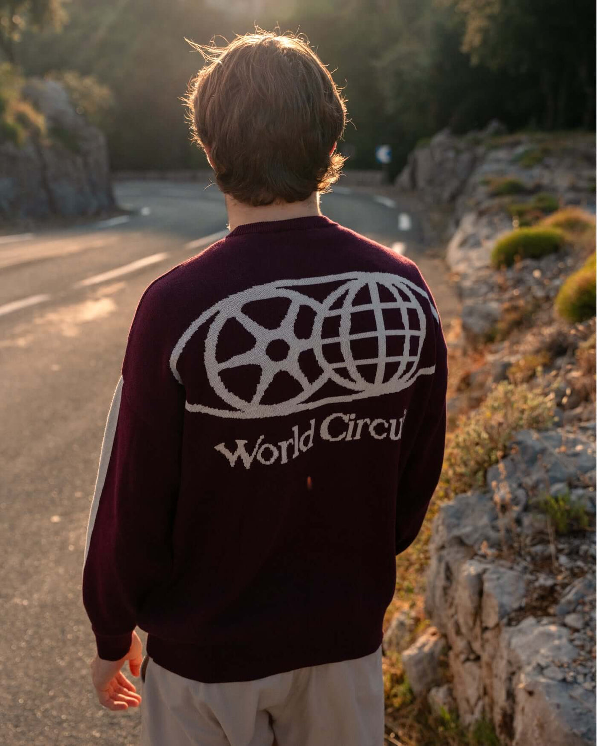 Person wearing the World Circuit Knitted Sweater - Burgundy, showcasing the globe emblem and jacquard motifs.