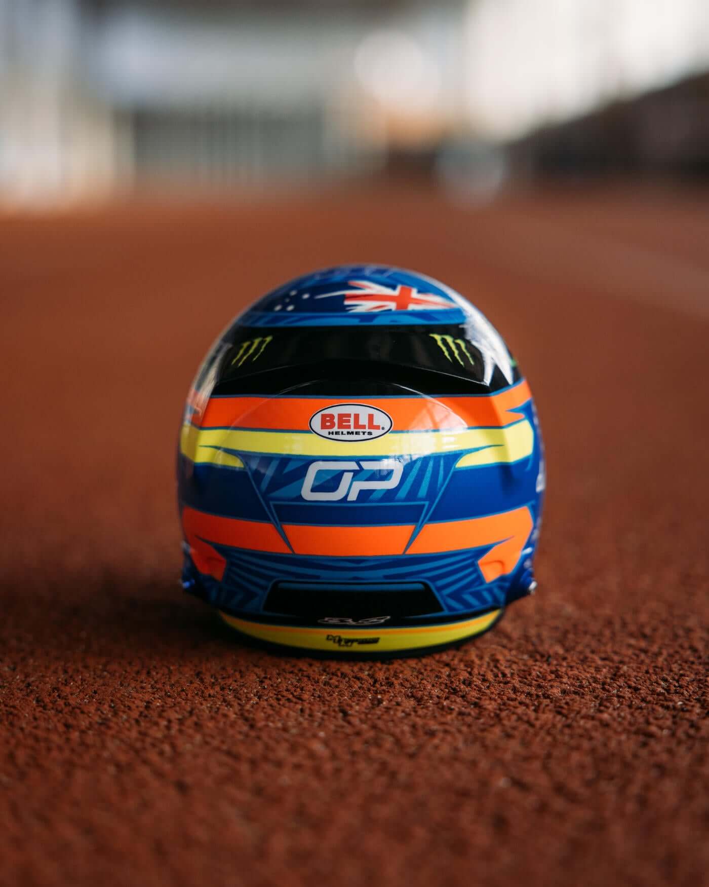 1:2 scale 2024 Season Oscar Piastri helmet with red, blue, and yellow design on a track by Bell.