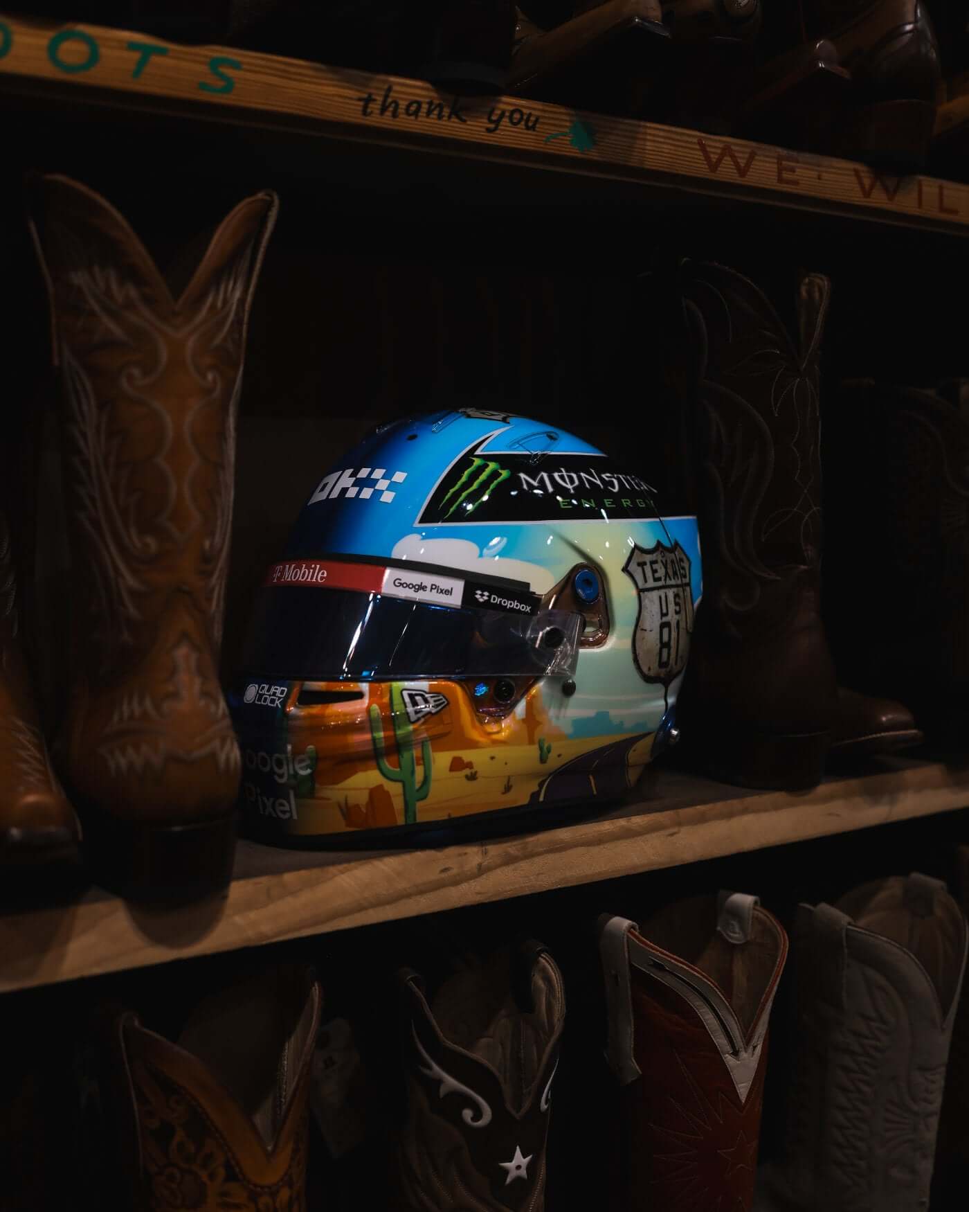 1:2 scale Oscar Piastri 2024 US Grand Prix helmet replica by Bell showcased among boots on a shelf.