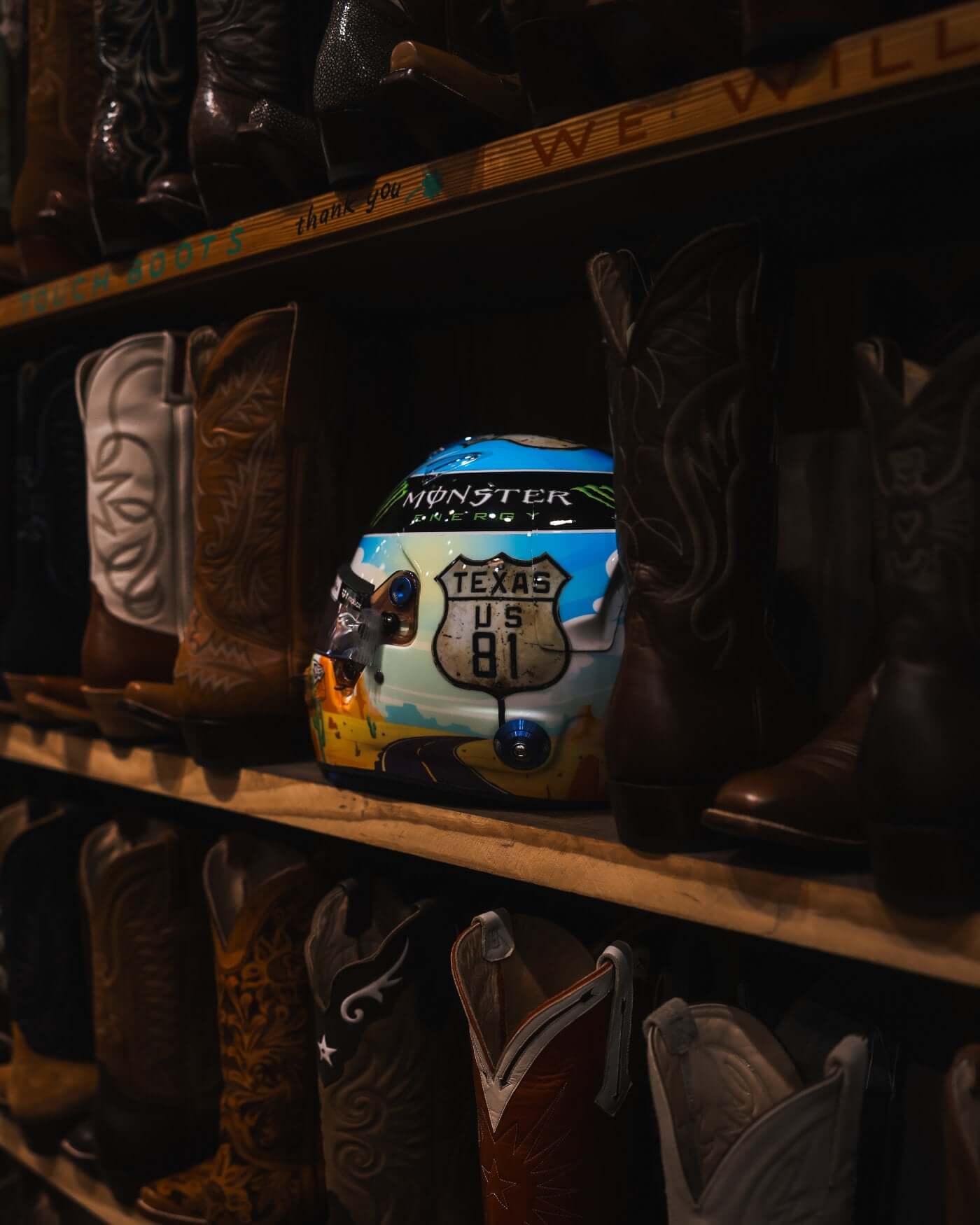 1:2 scale 2024 Oscar Piastri US helmet replica displayed among cowboy boots, featuring Texas US Grand Prix design.