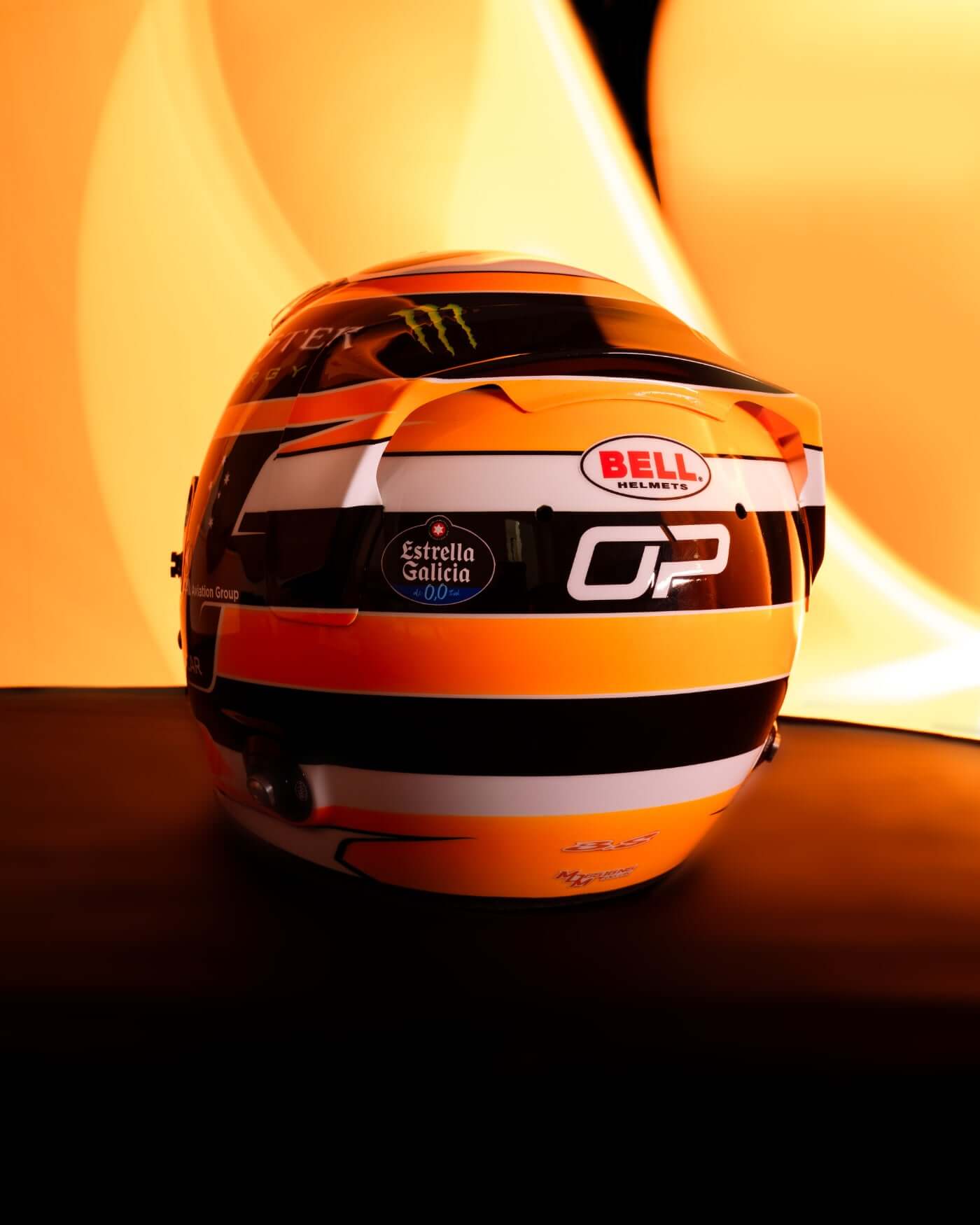 Rear view of a 1:2 scale Oscar Piastri 2025 Monaco helmet by Bell, showcasing iconic papaya colors and his logo.