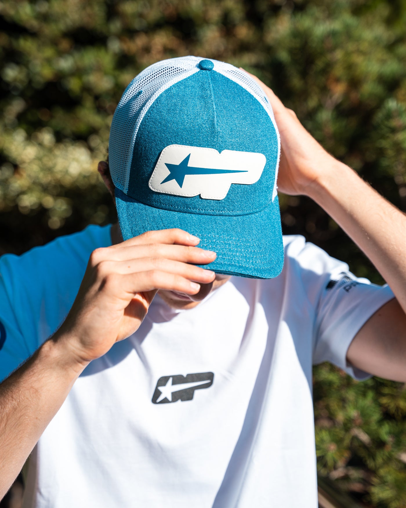 A person wearing the Origins Cap, a retro 5 panel trucker hat with a leather-look OP patch and breathable mesh.