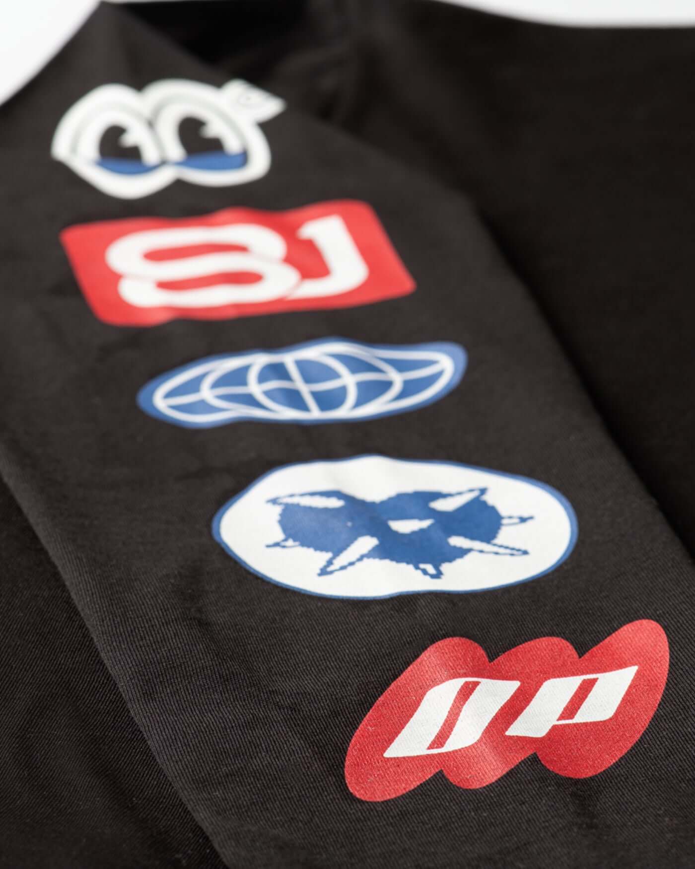 Close-up of the sleeve graphics on the Origins Long Sleeve T-Shirt - Black, featuring bold colorful patches.