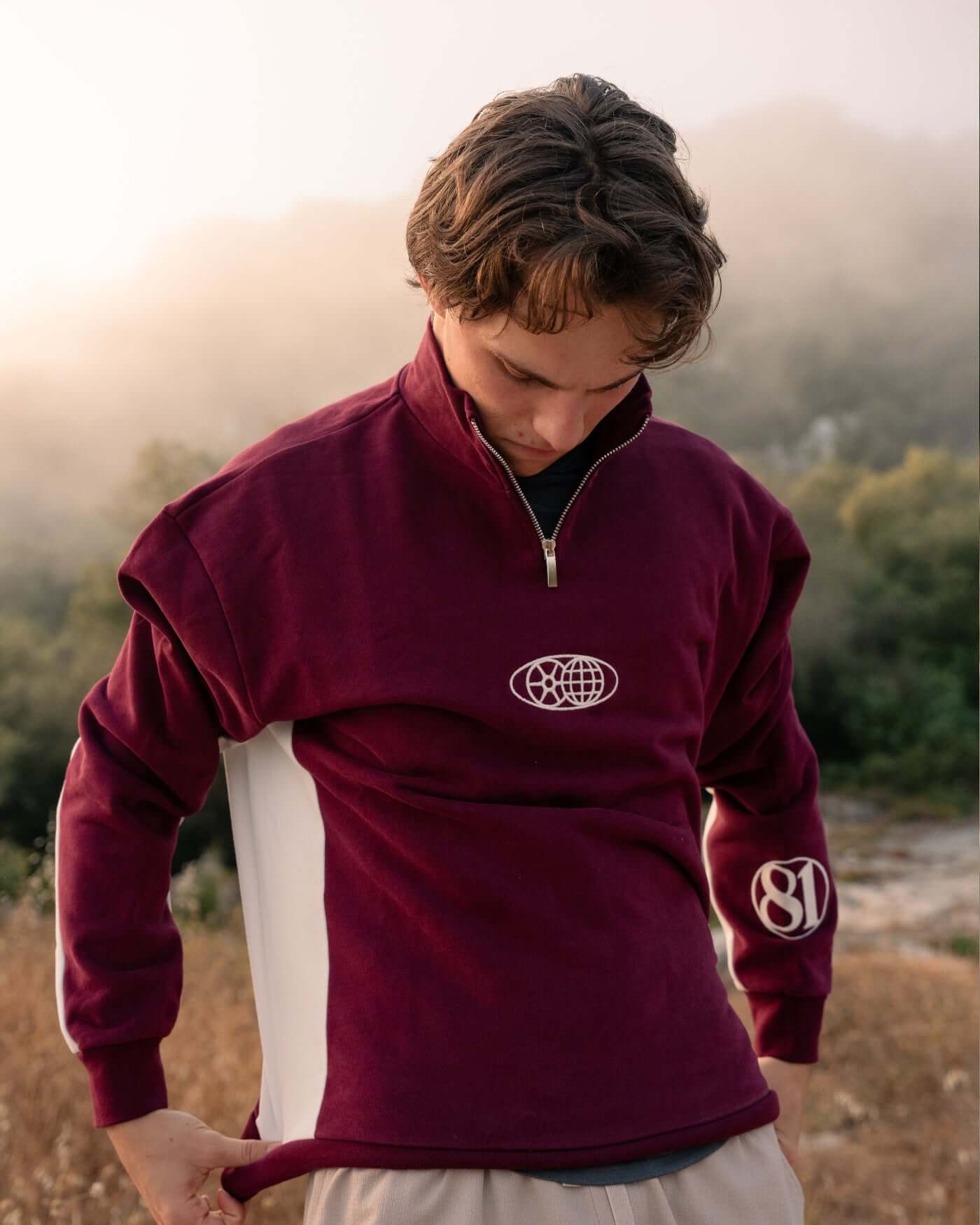 Model wearing the World Circuit Quarter Zip - Burgundy with off-white side panels and globe emblem.