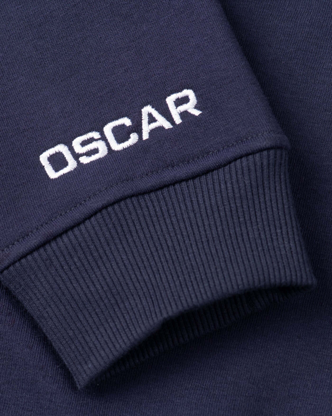 Close-up of Oscar's logo embroidered on the cuff of the navy Signature Sweater.