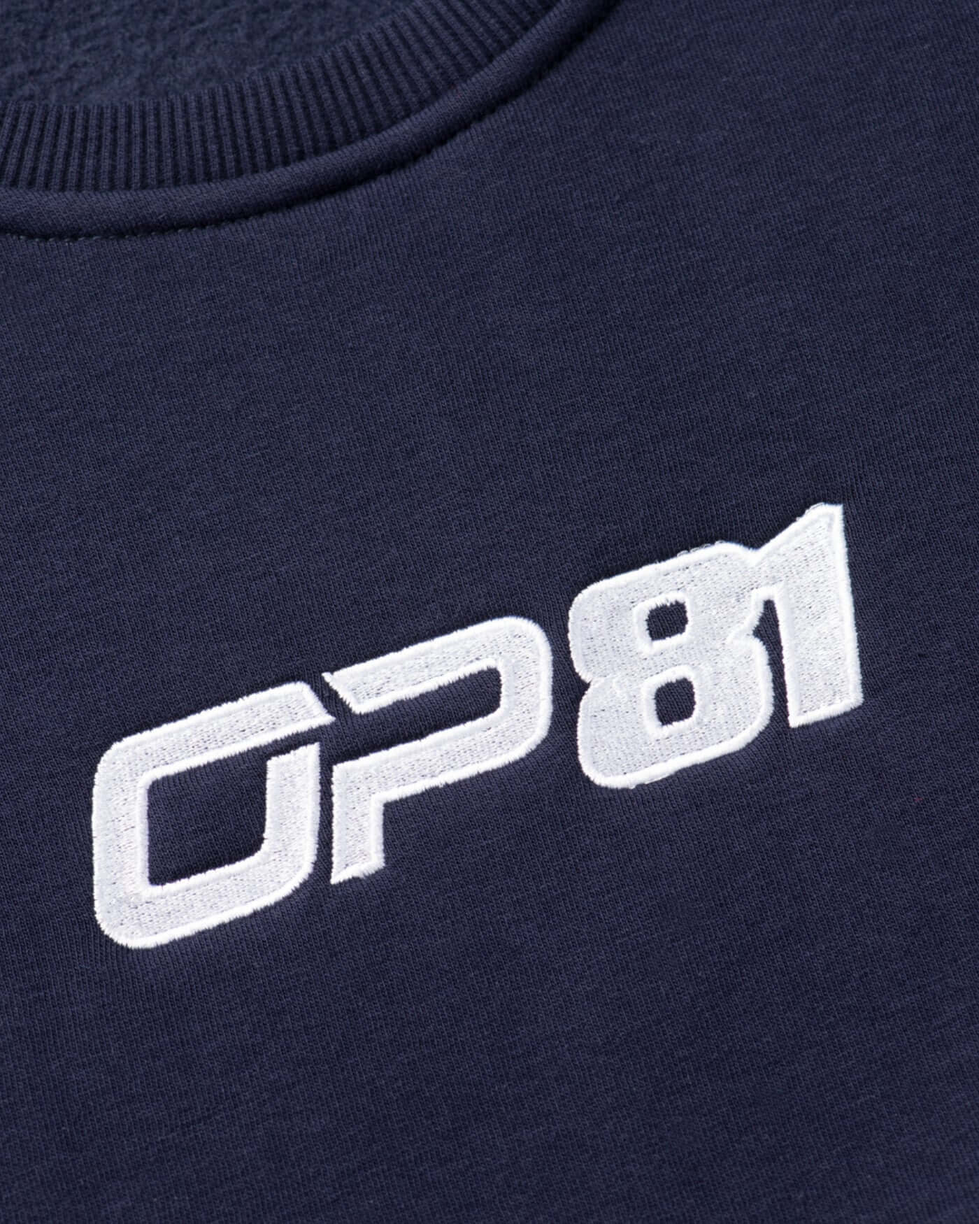 Close-up of OP81 embroidered logo on navy fleece-lined signature sweater.