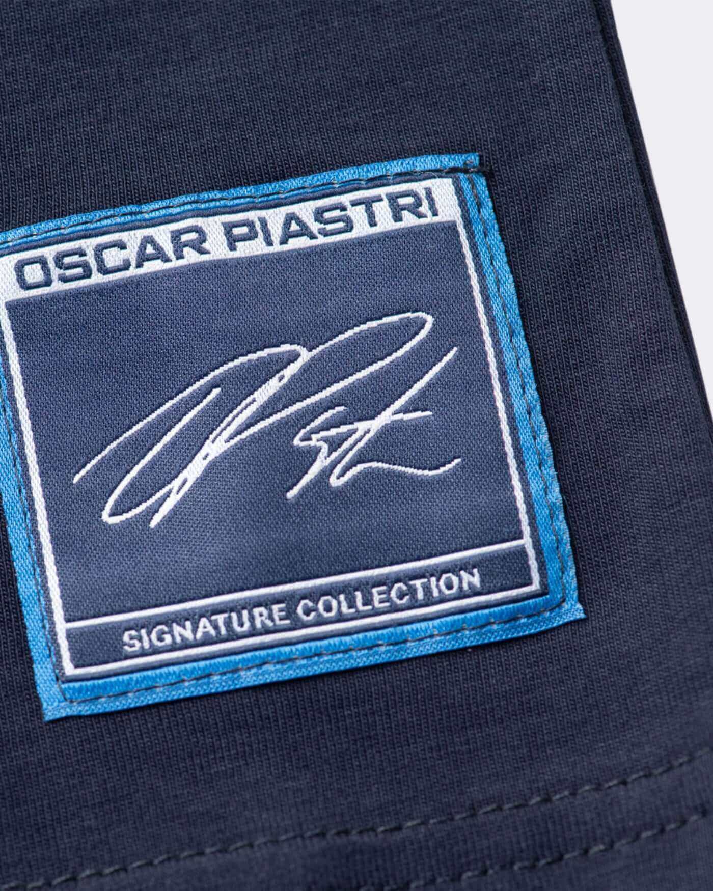Close-up of the Oscar Piastri signature logo patch on a navy t-shirt from the Signature Collection.