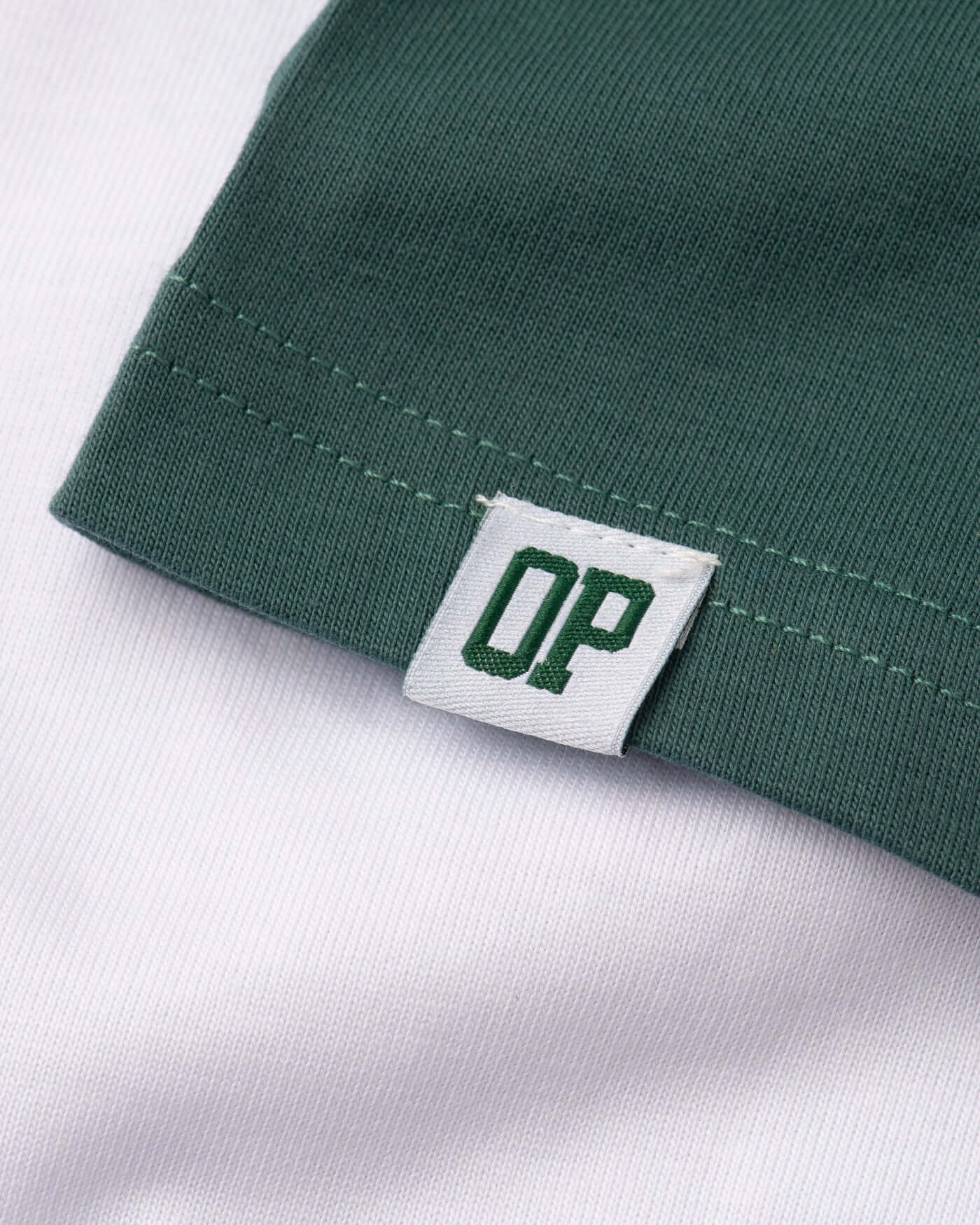 Close-up of green and white Home Race T-Shirt, featuring a tag with 'OP' branding, showcasing quality stitching detail.