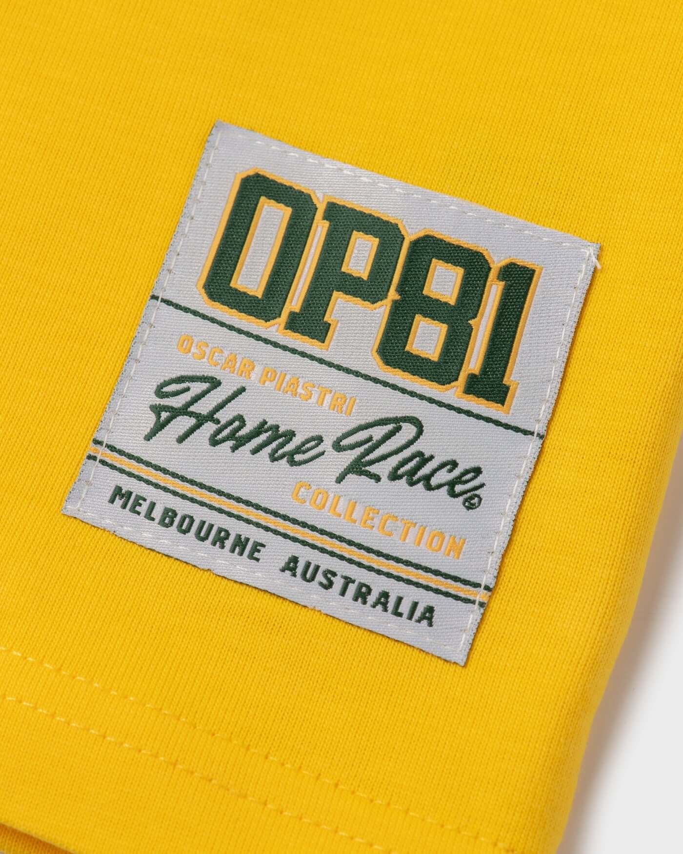Close-up of Home Race T-Shirt label in yellow, featuring Oscar Piastri's OP81 Collection from Melbourne, Australia.