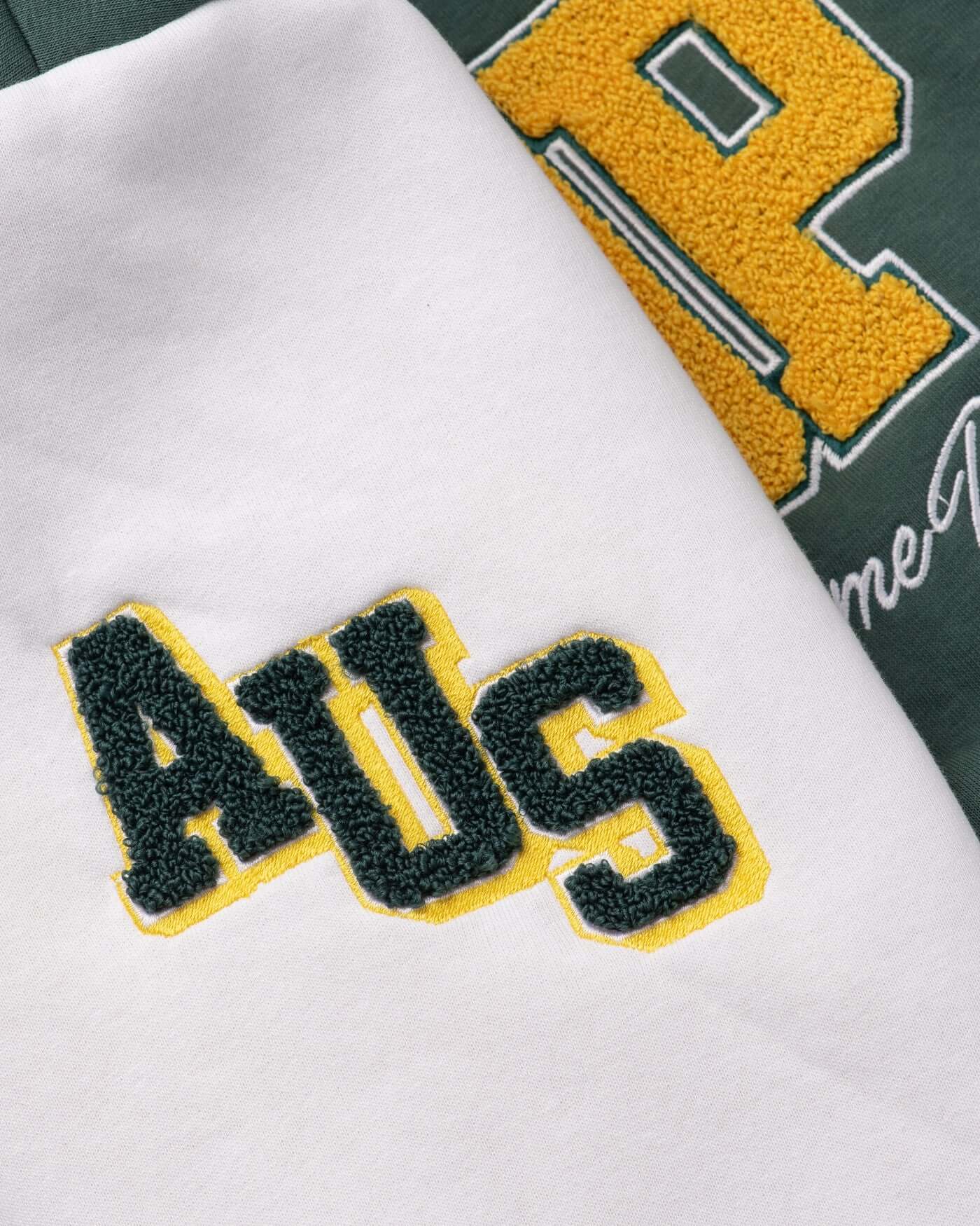 Close-up of luxurious chenille embroidery patches on a varsity jacket featuring 'AUS' lettering in green and yellow.