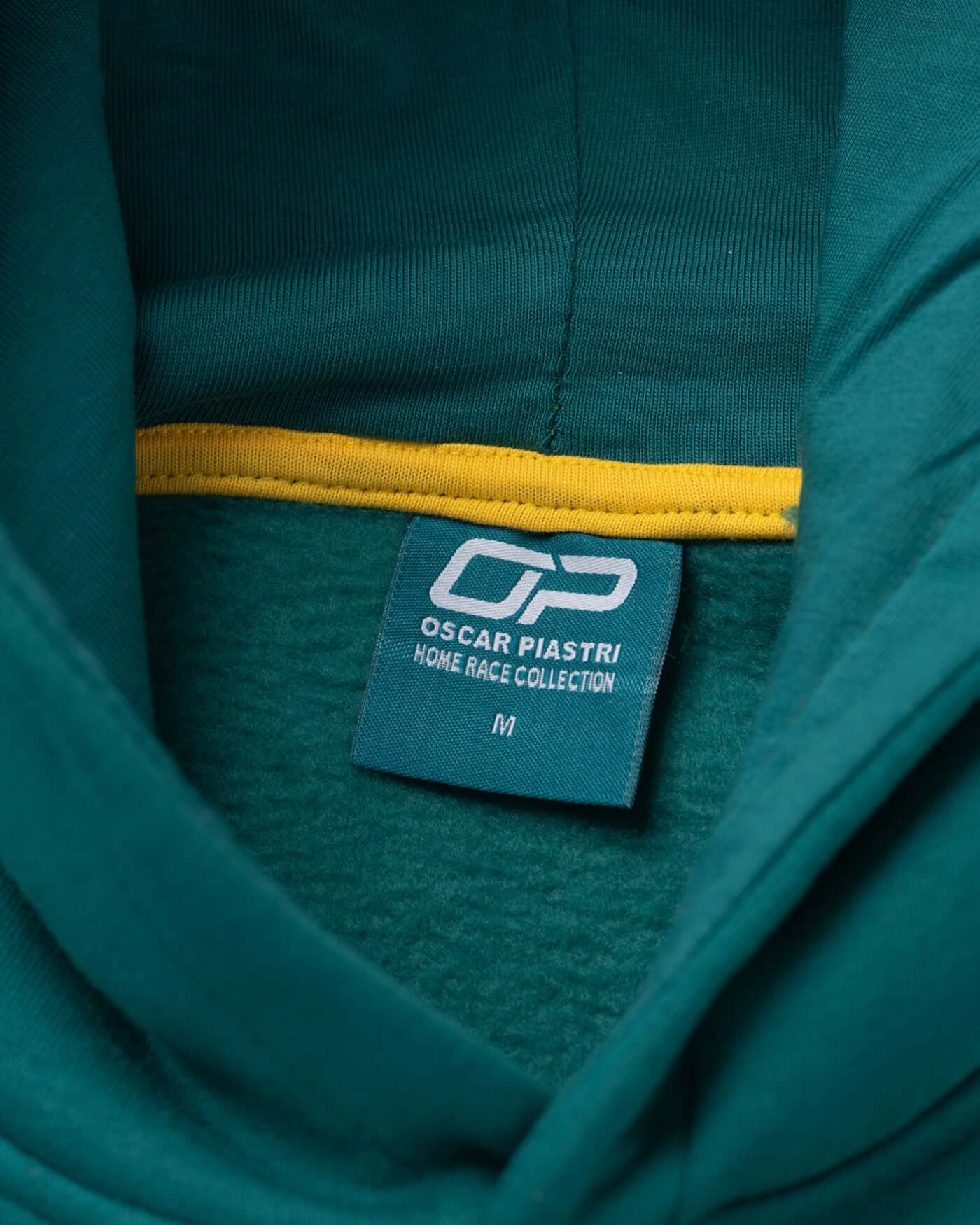 Home Race '26 Hoodie - Green tag detail showing Oscar Piastri branding and the cozy inner lining.