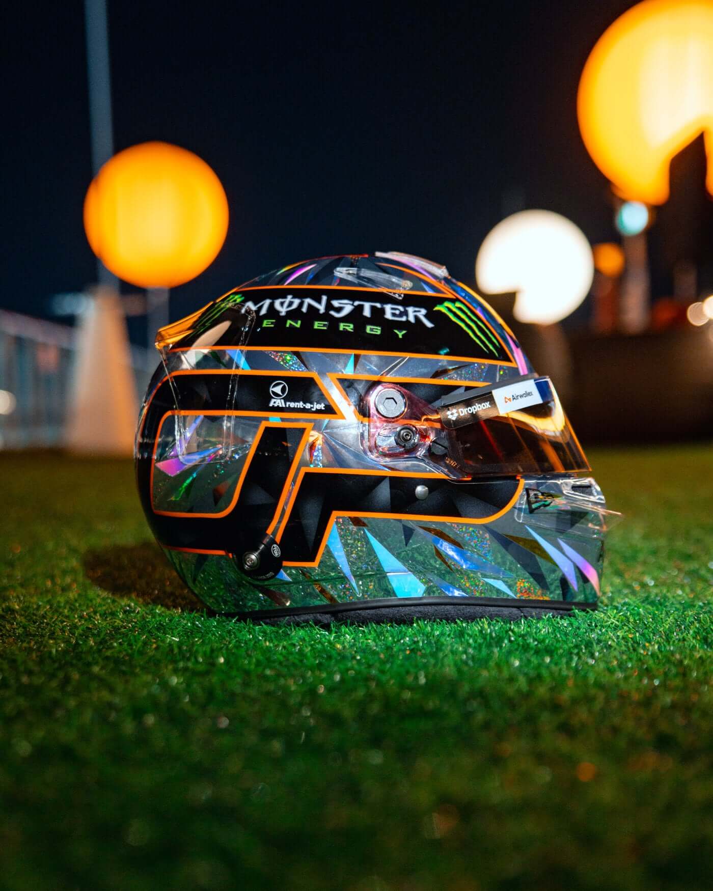 1:2 scale 2024 Singapore Helmet - Oscar Piastri on grass at night with glowing orange lights in background.