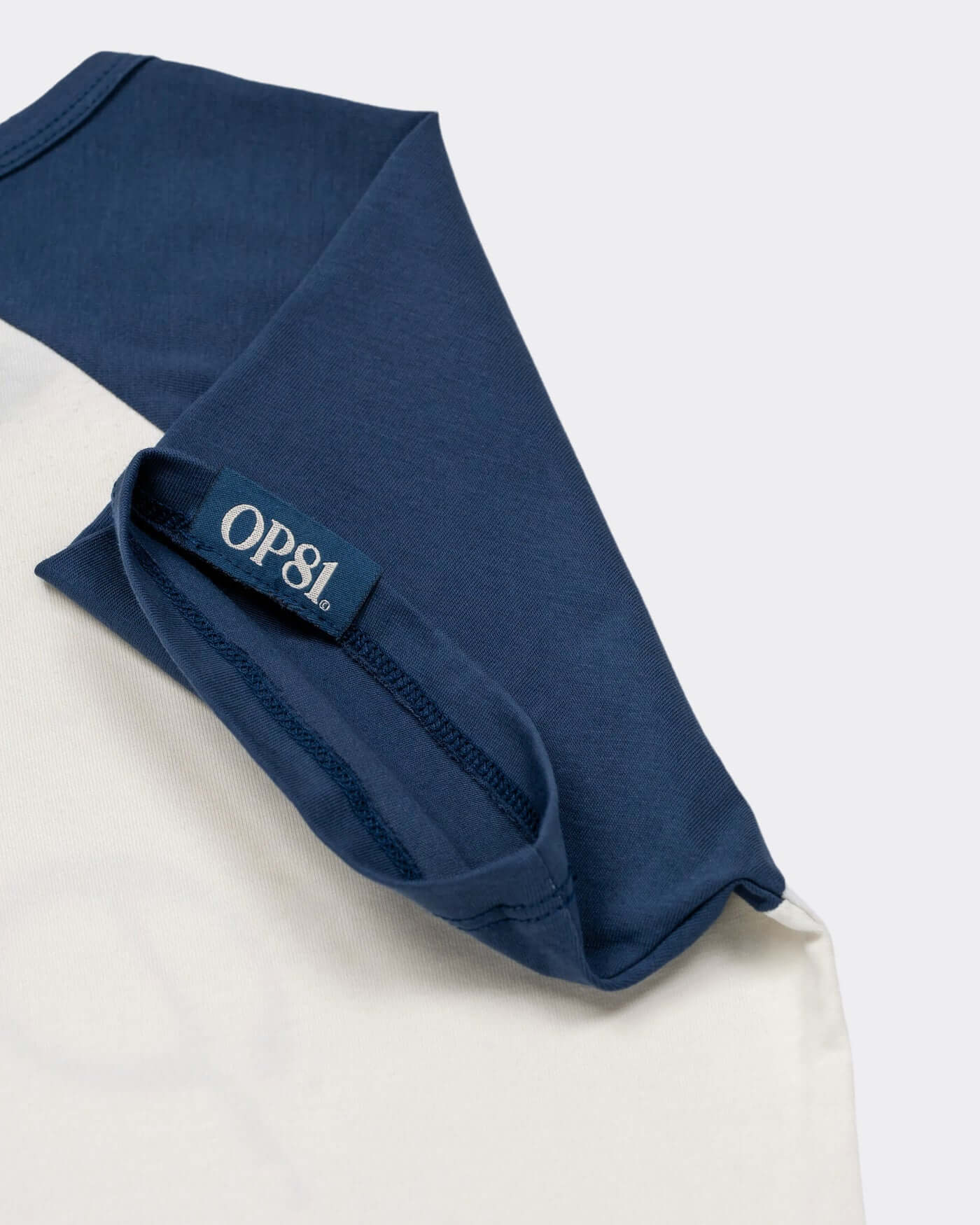 Close-up of the World Circuit Crop Tee showcasing blue raglan sleeves and OP81 tag detail.