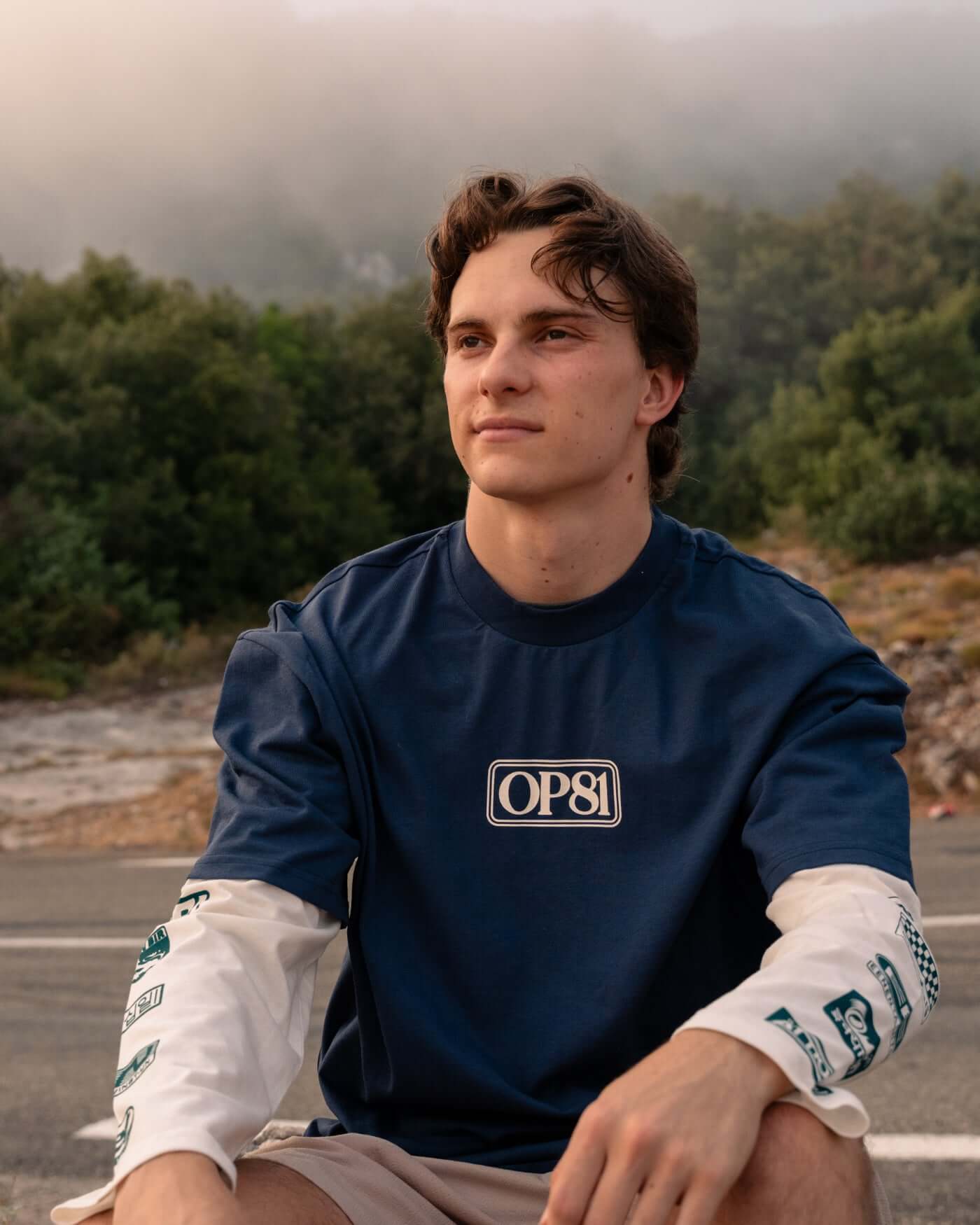 World Circuit Layered T-Shirt - Blue worn by a young man outdoors with a serene background.