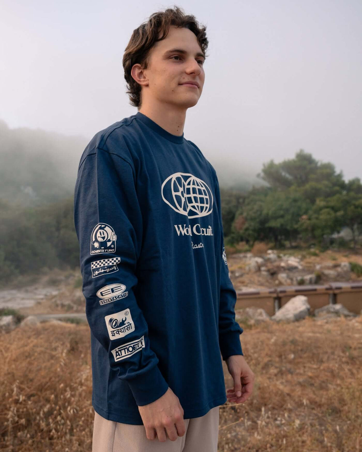 Model wearing World Circuit Long Sleeve T-Shirt - Blue, showcasing globe design and printed graphics on sleeves.