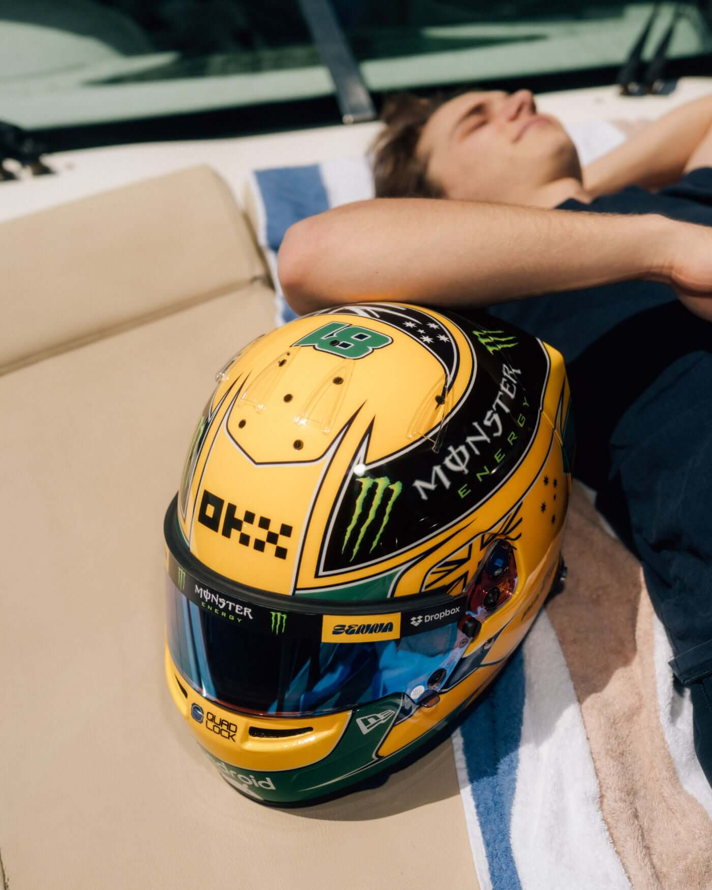 Oscar Piastri laying next to the 1:2 scale replica of the 2024 Monaco Grand Prix Ayrton Senna tribute helmet.