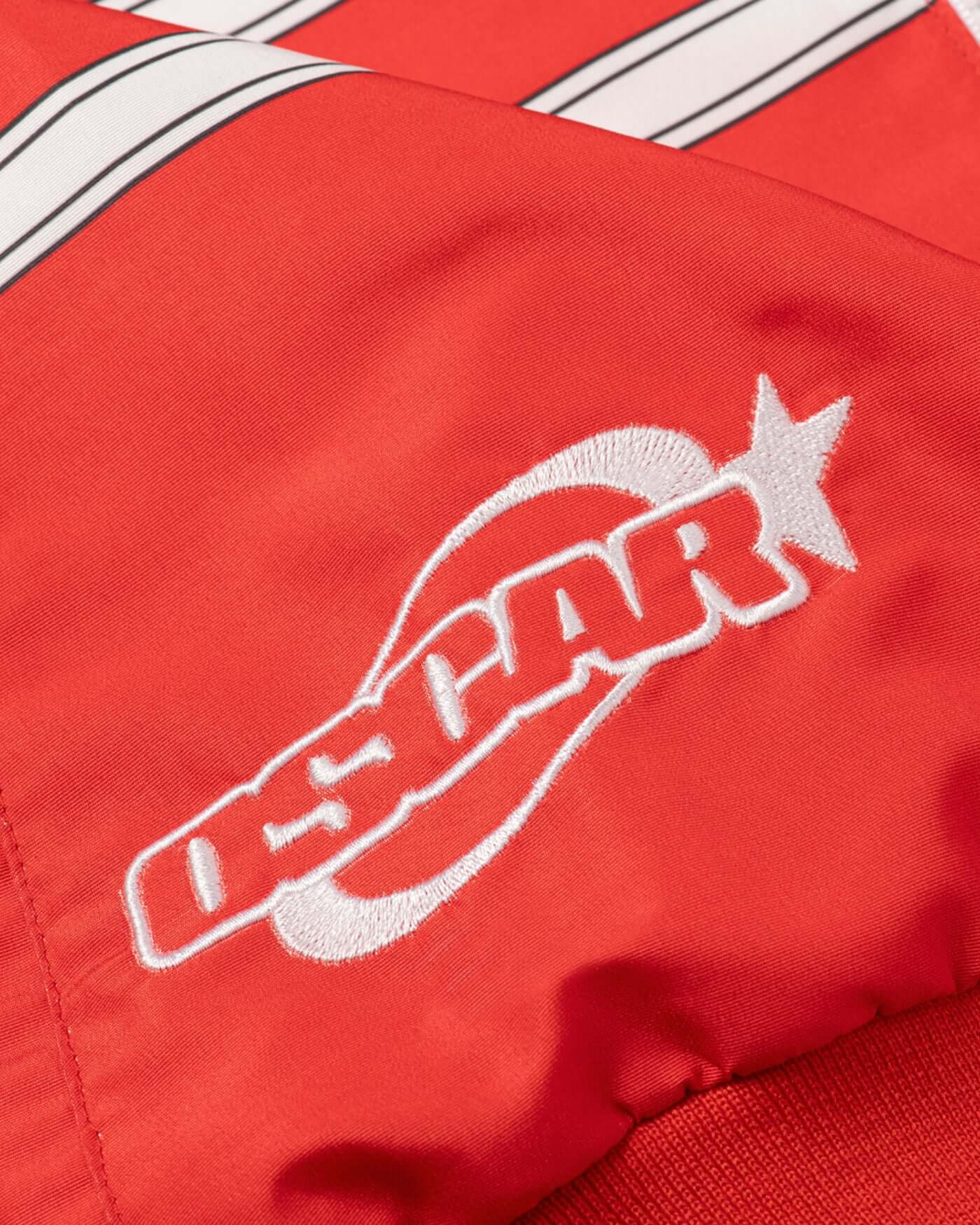 Close-up of the embroidered logo on the Origins Race Jacket with bold red fabric and retro details.