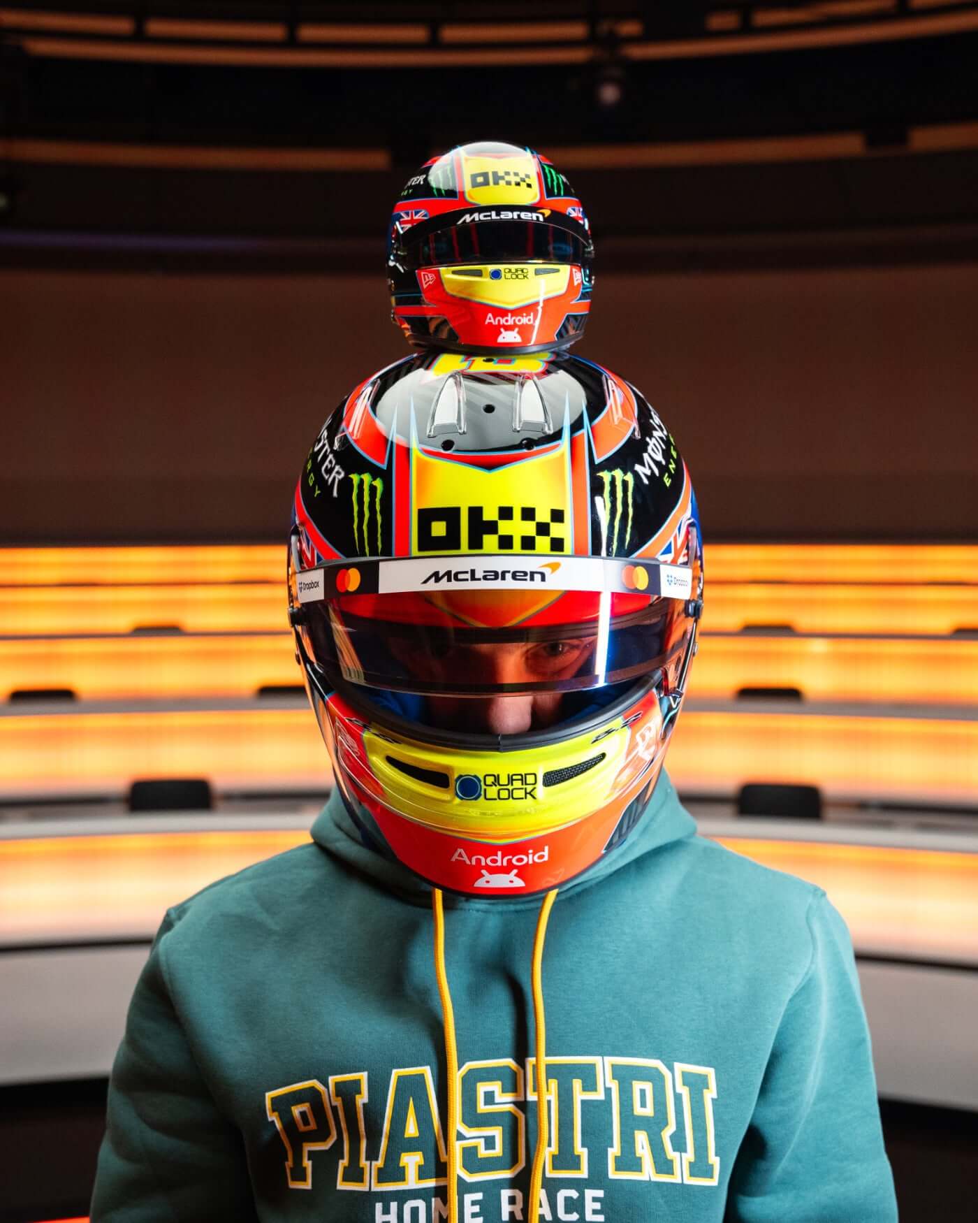 1:2 scale Oscar Piastri F1 helmet replica displayed with a fan wearing a hoodie, showcasing McLaren design.