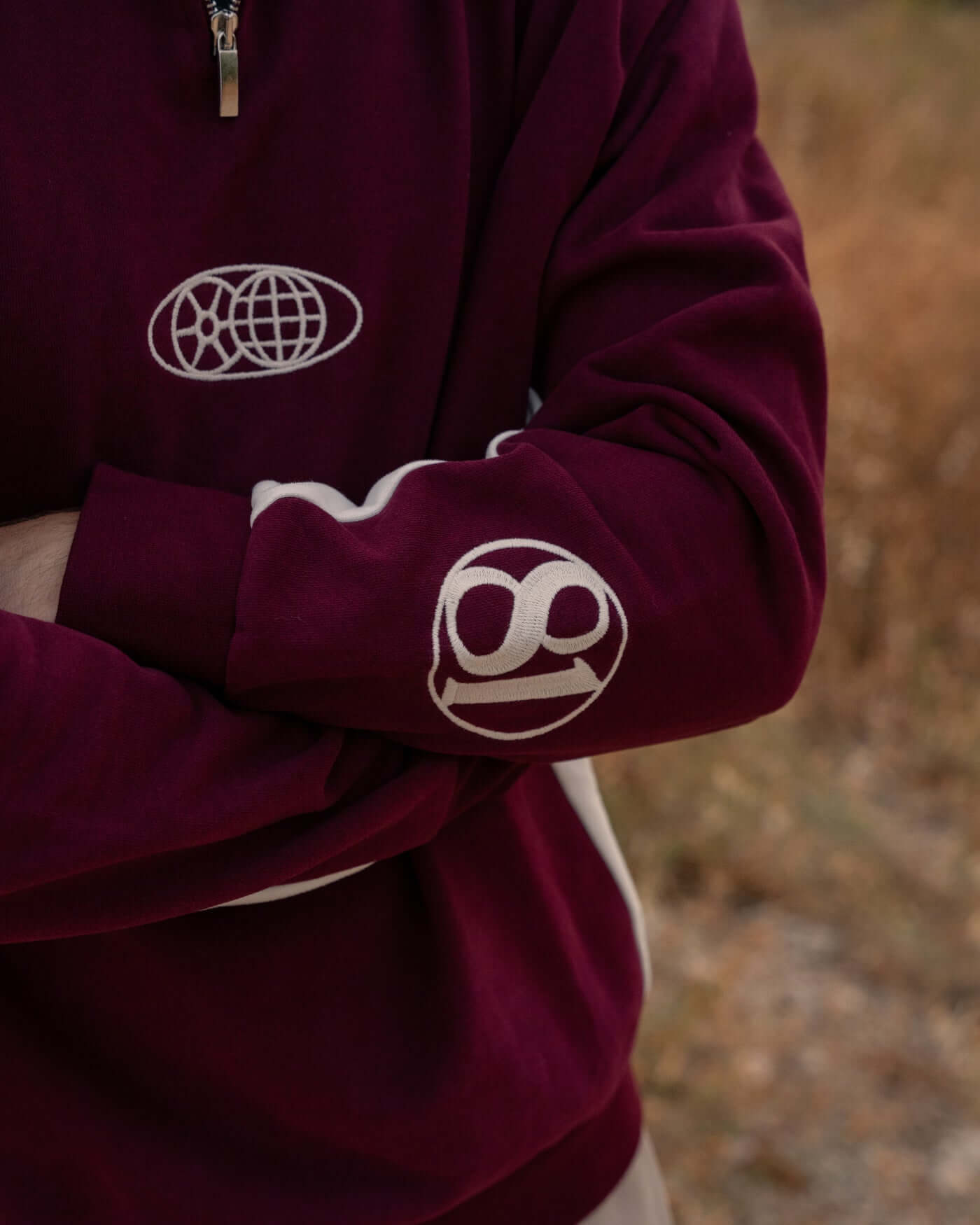 Close-up of the World Circuit Quarter Zip - Burgundy showcasing globe emblem and Oscar Piastri signature.