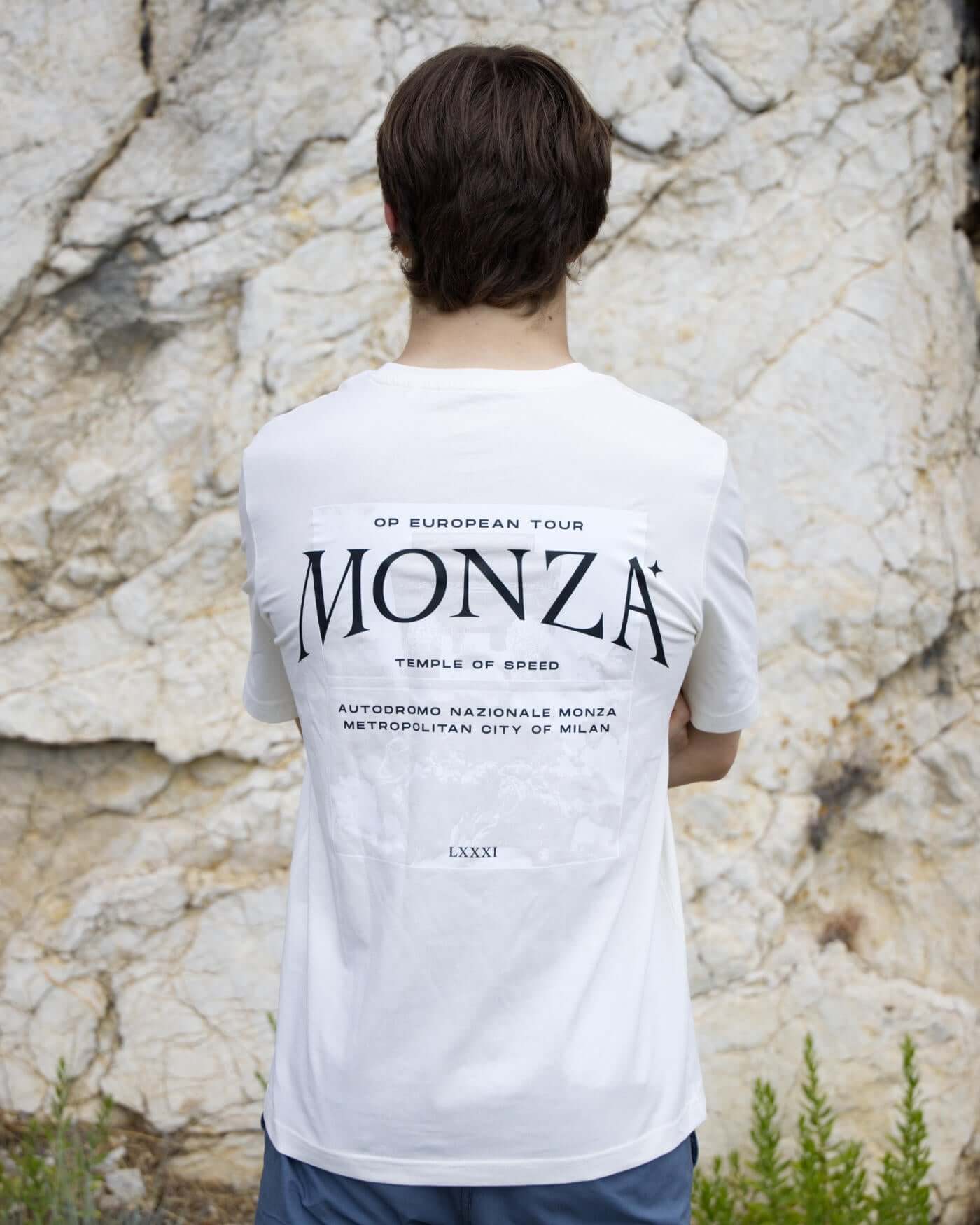 Oscar wearing Monza T-Shirt in off white, featuring back print with "Temple of Speed" text, standing against a stone backdrop