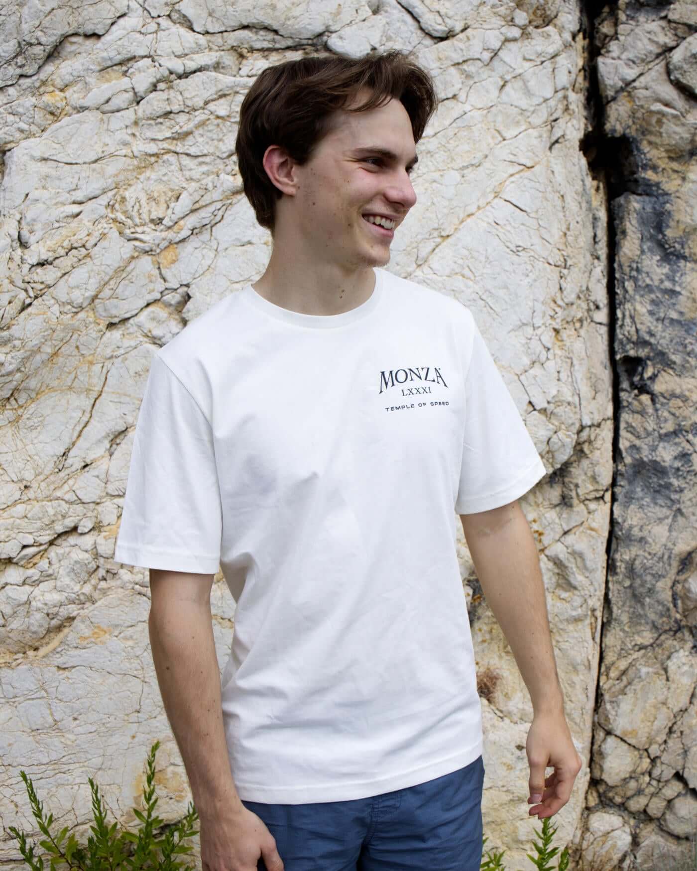 Oscar wearing Monza T-Shirt in off white with ribbed neck collar, standing outdoors by a rock wall.