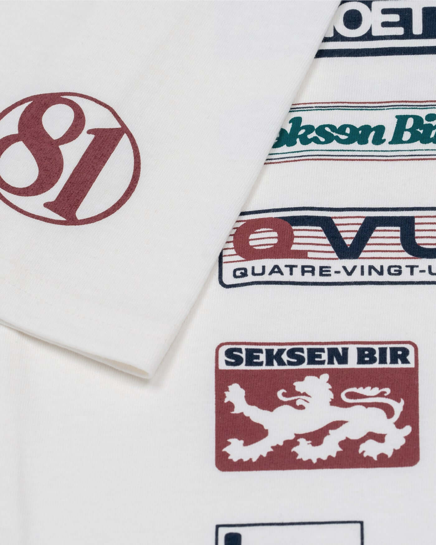 Close-up of the World Circuit T-Shirt - Off White featuring globe emblem, 81 on sleeve, and international sponsor graphics.