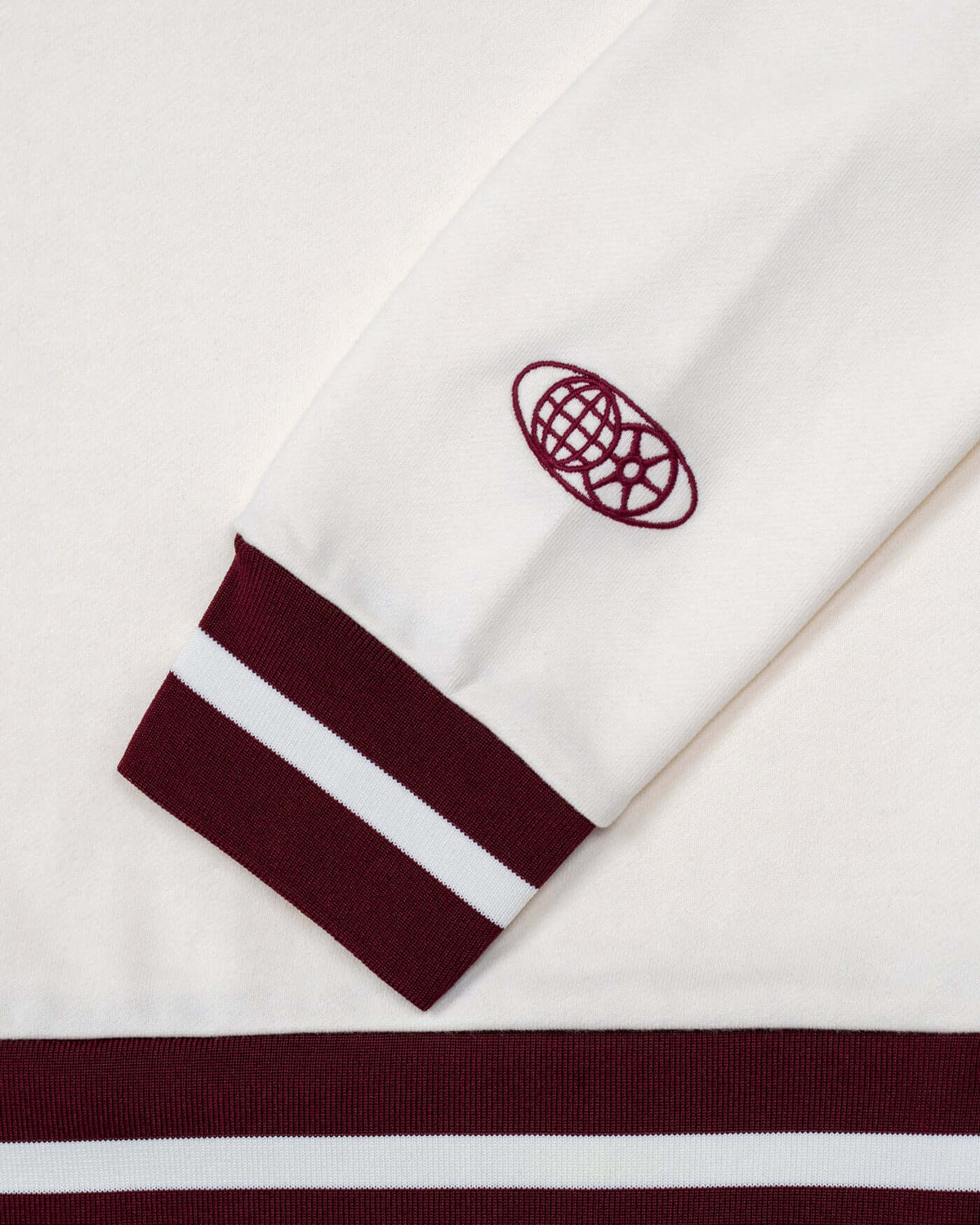 World Circuit Women's Sweater - Off White detail showcasing burgundy globe emblem and striped cuffs.